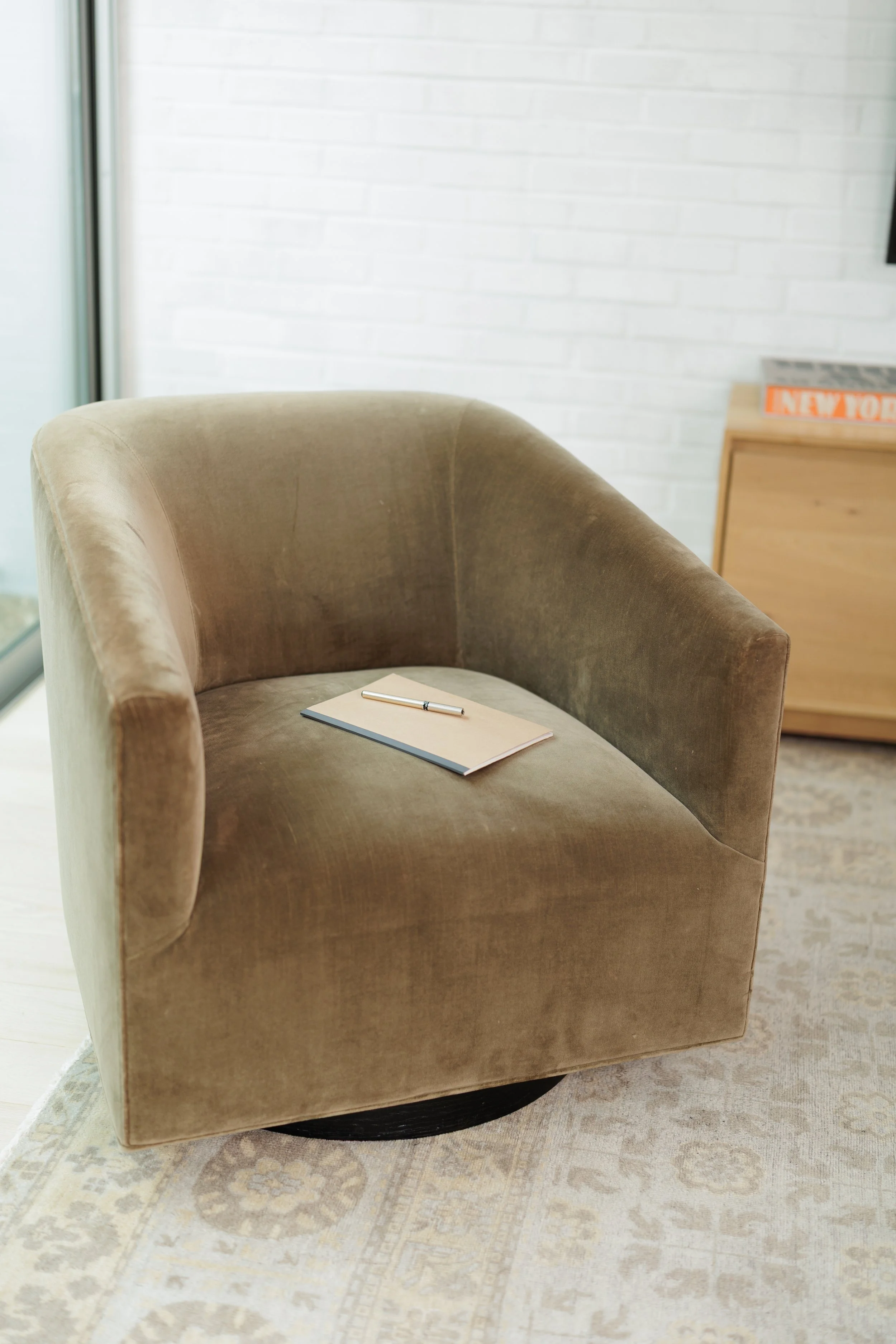 olive taupe colored chair with notebook and pen atop of the chair