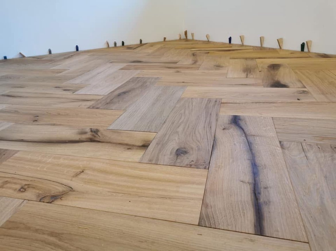 Newly installed wooden flooring in a room with a white wall.