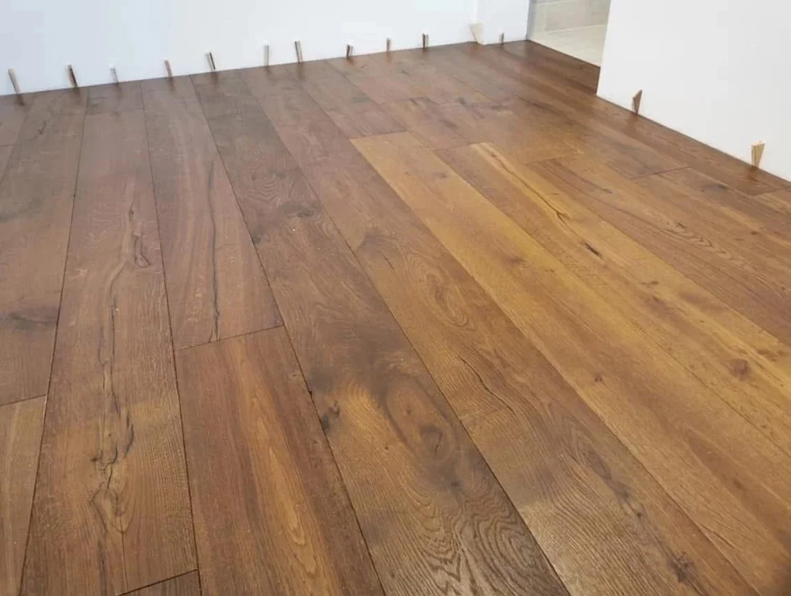 Close-up view of a newly installed wooden floor in a room with no furniture, showing the wood grain and texture.