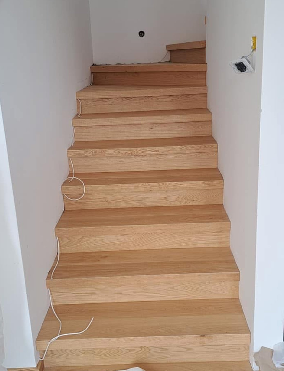 Wooden staircase with unfinished walls and electrical wiring visible.