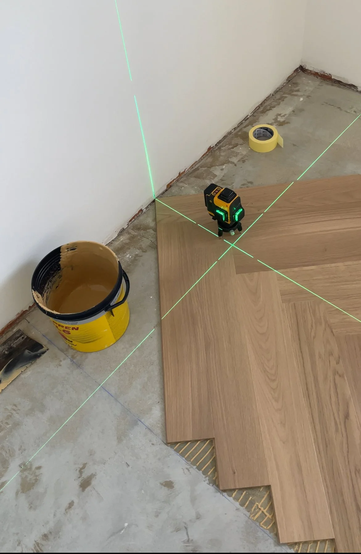 Laserska libela, ki projicira zelene črte na vogal sobe, na katero so nameščena lesena tla.