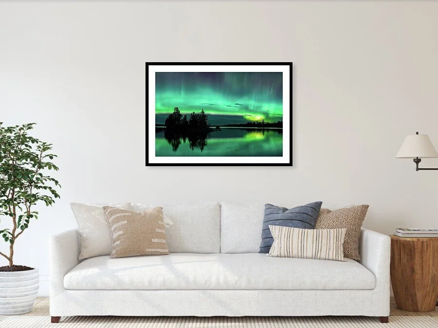 A framed print of the northern lights over a lake, hanging on a white living room wall.