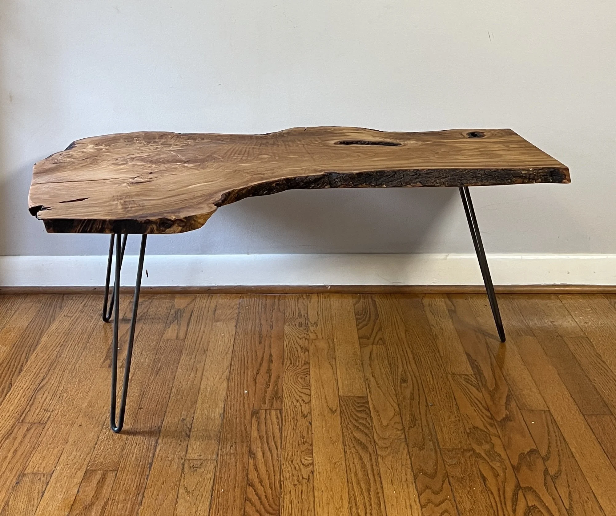 A rustic wooden table with black metal hairpin legs against a white wall and wooden floor.