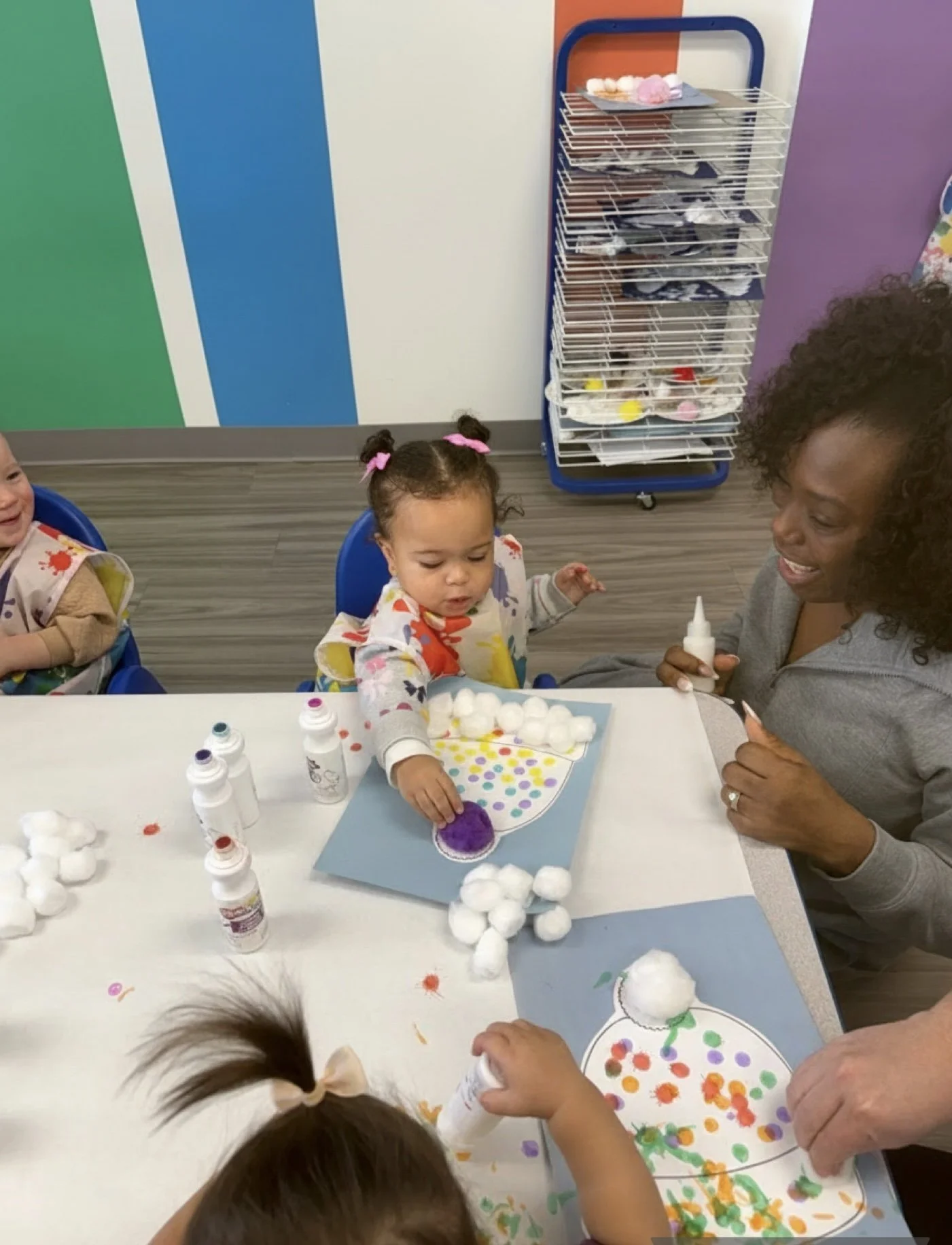 Mom smiling as her toddler creates a winter hat art project with paint dabbers during a Kid Ka Doodle Dabble Doodlers class in Hunterdon County NJ.