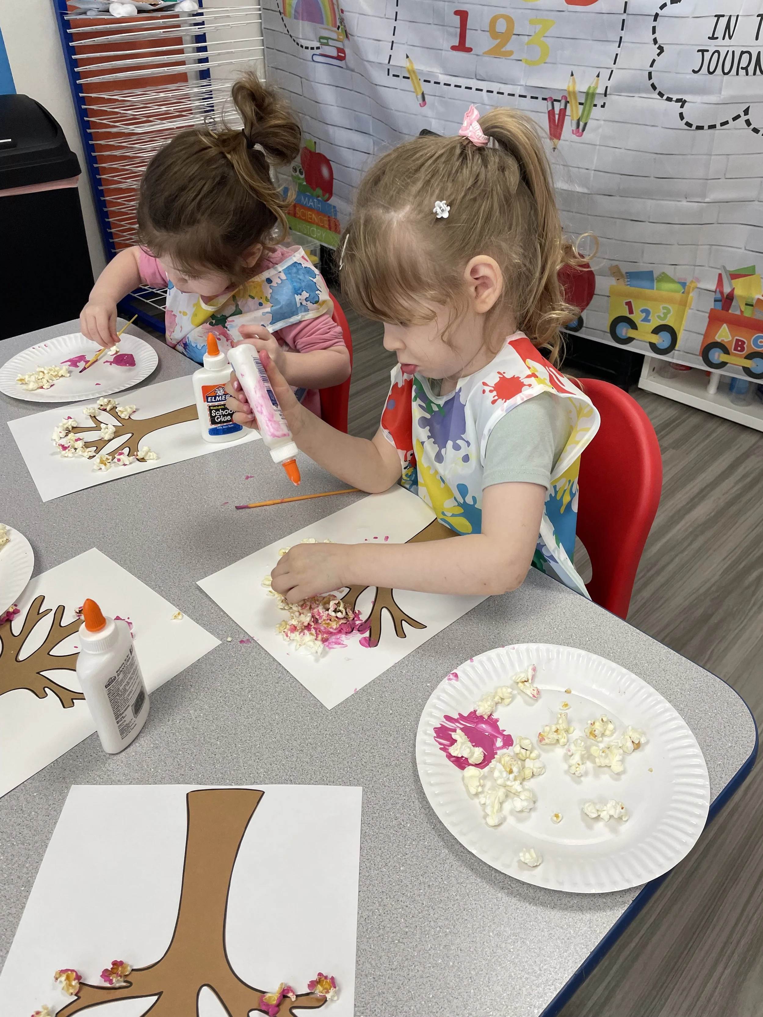 Children creating cherry tree artwork with paint and textured materials during a Kid Ka Doodle Pre Doodlers class.