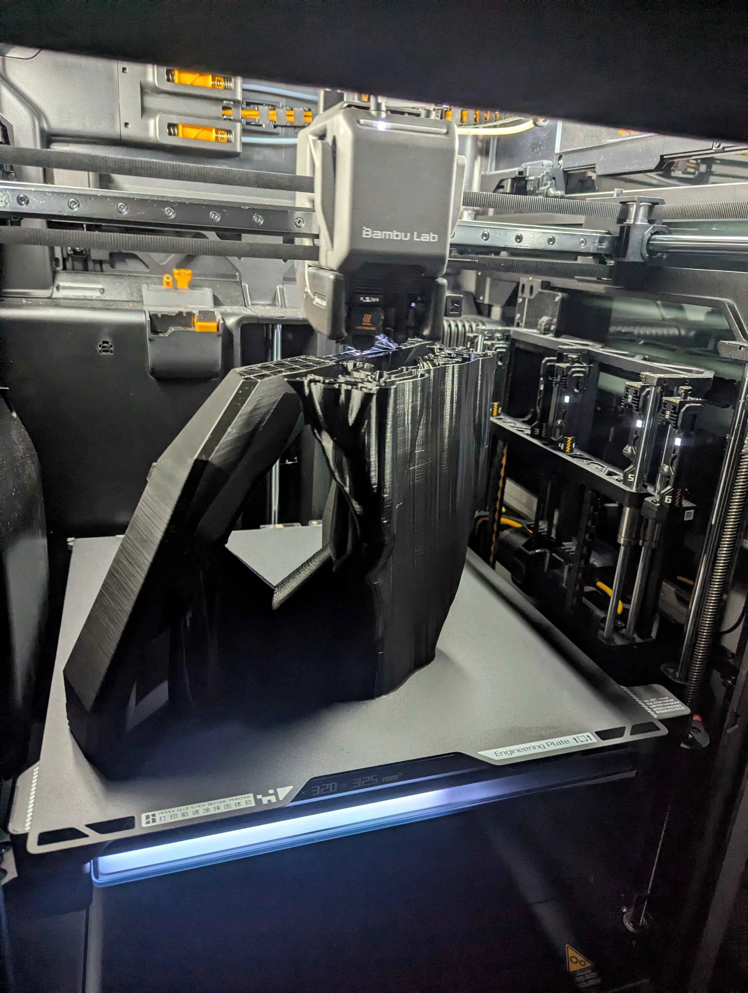 3D-Drucker beim Drucken eines schwarzen Objekts mit einem Bamboo Lab Druckkopf, mit sichtbarem Bauraum und technischen Komponenten.