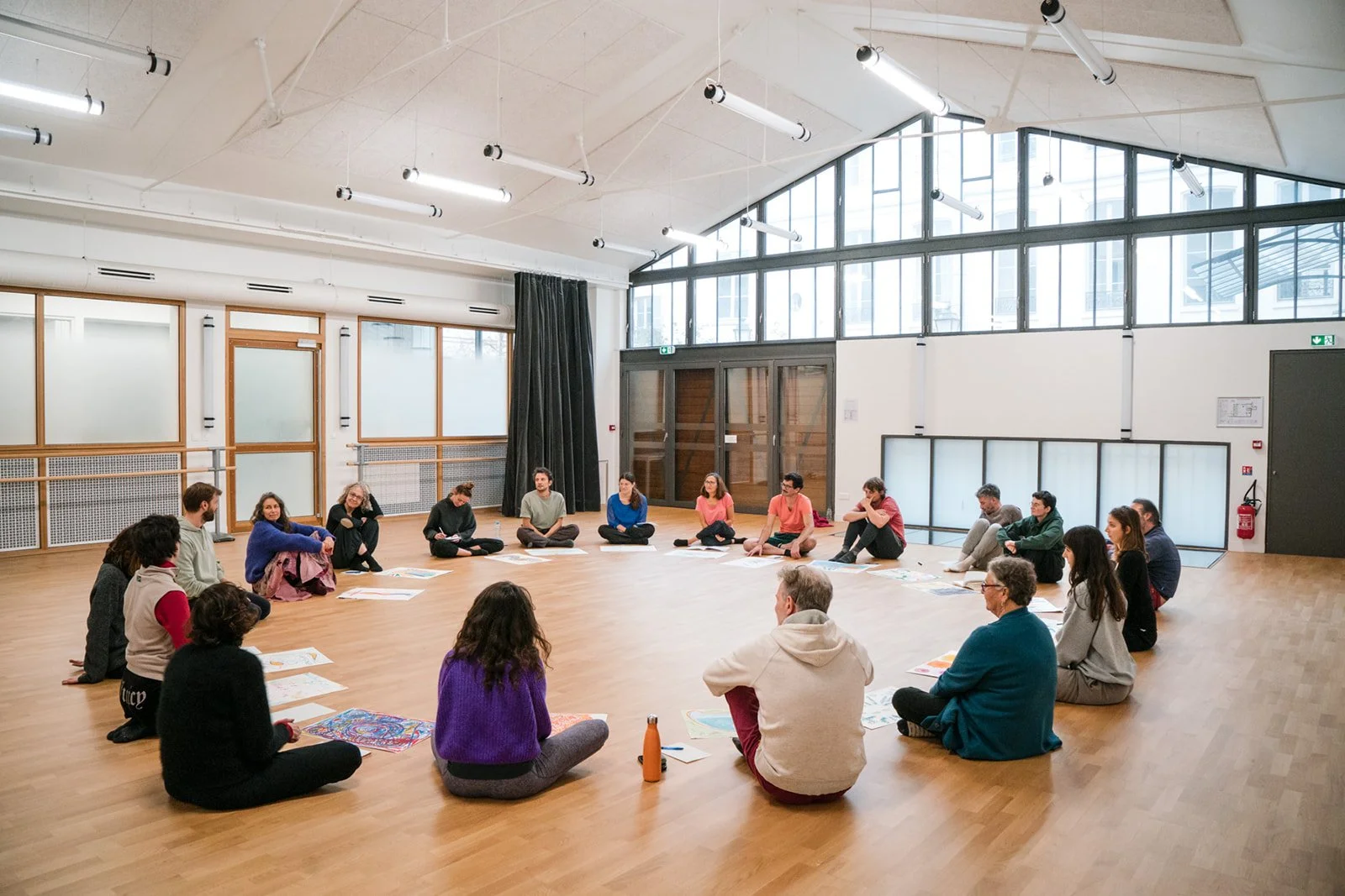 Groupe de personnes assises en cercle dans une salle lumineuse avec de grandes fenêtres et un sol en bois, lors des dimanches Life Art Process® de Stéphane Vernier.