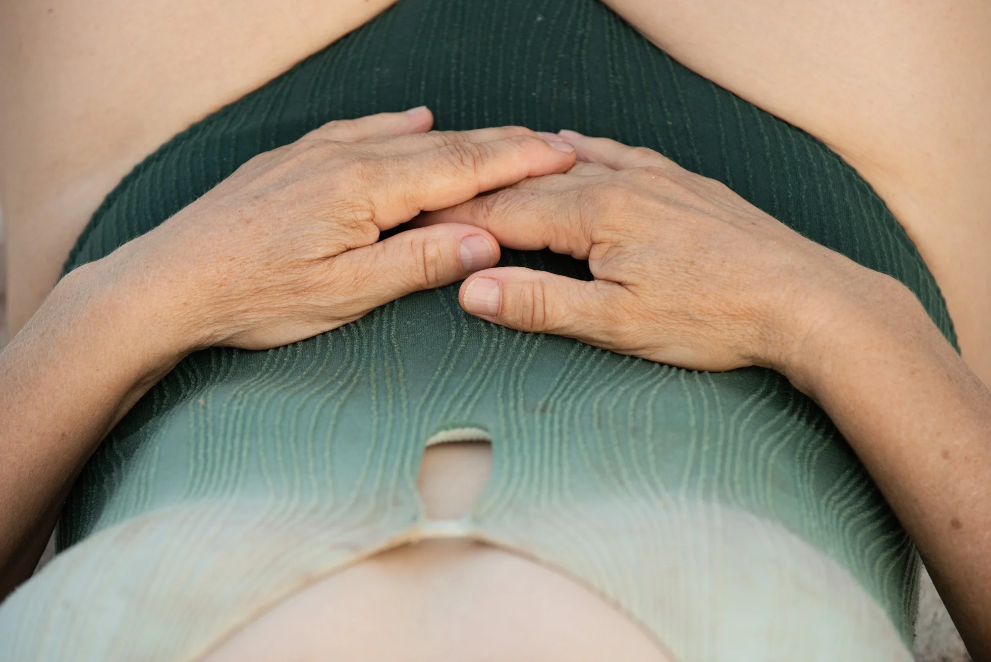 Mains posées sur le ventre d'une personne portant un haut vert, lors du stage Nature.s avec Stéphane Vernier et Isabelle Chapuis.