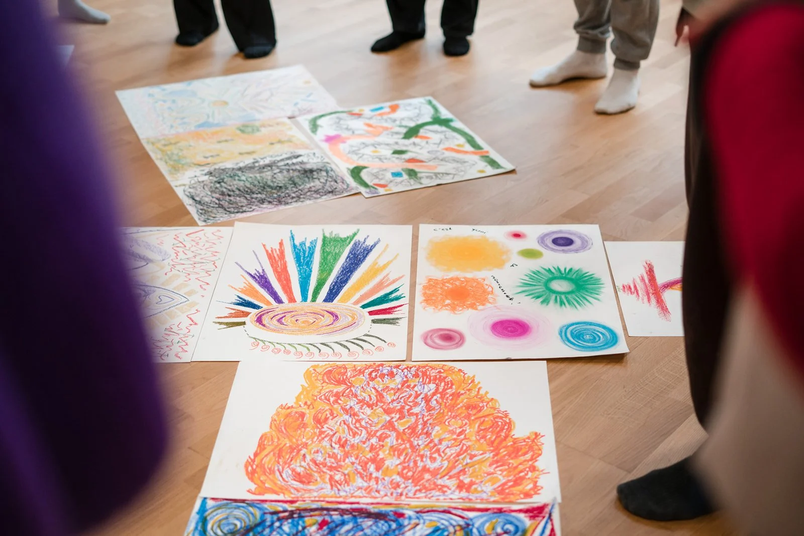 Dessins d'enfants colorés exposés au sol avec des personnes debout autour, lors des dimanches Life Art Process® de Stéphane Vernier.