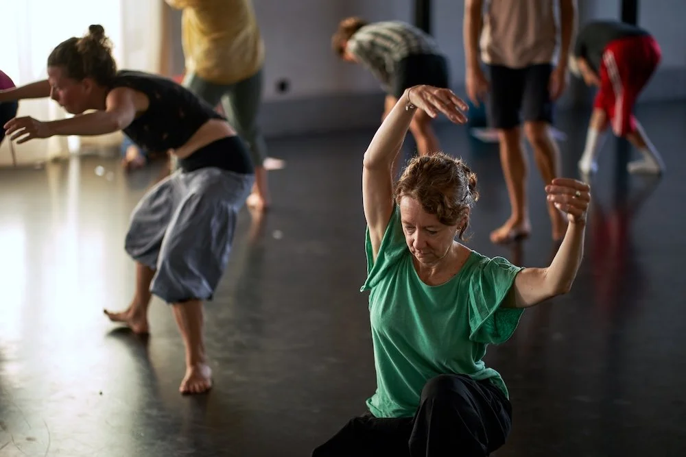 Un groupe de personnes dansant dans une salle sombre, avec une lumière naturelle venant d'une fenêtre, lors d'un atelier Life Art Process®.