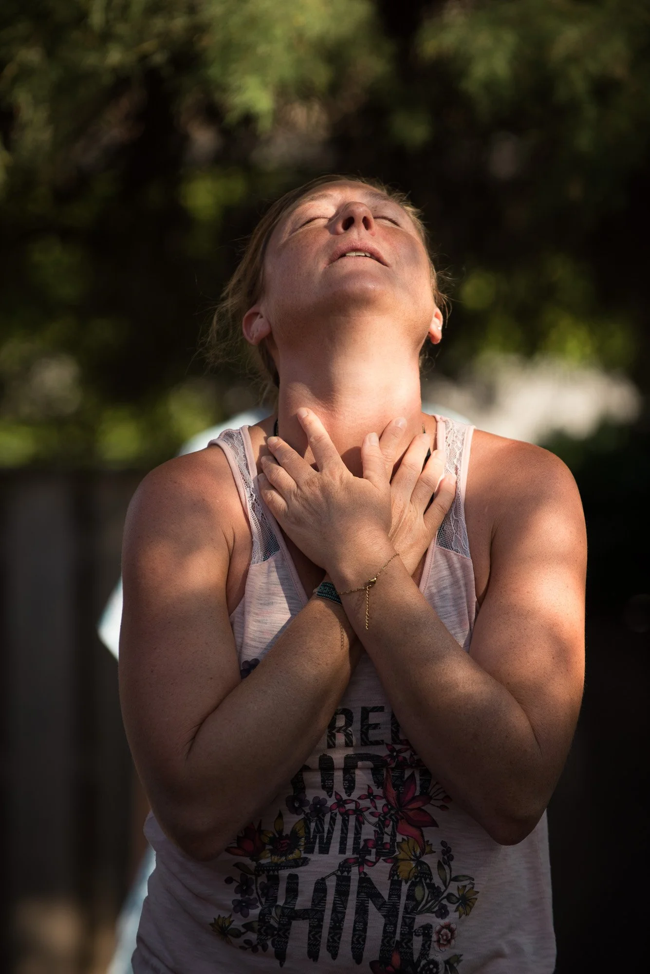 Une femme éprouve une émotion intense dans sa danse, les mains sur la gorge et la tête levée, dans un environnement extérieur avec des arbres en arrière-plan.