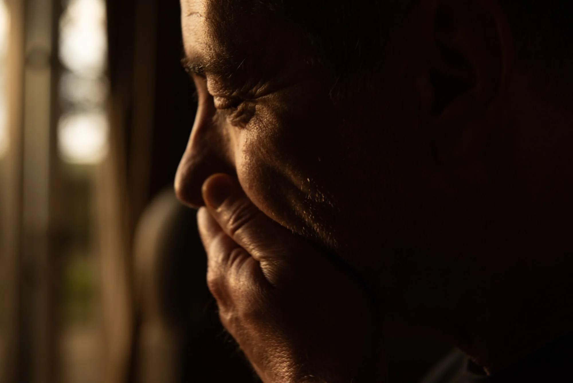 Un homme en profil avec la main sur le visage, éclairage chaud venant de la gauche, ambiance sombre et introspective, lors du stage Regards animé par Isabelle Chapuis et Stéphane Vernier.