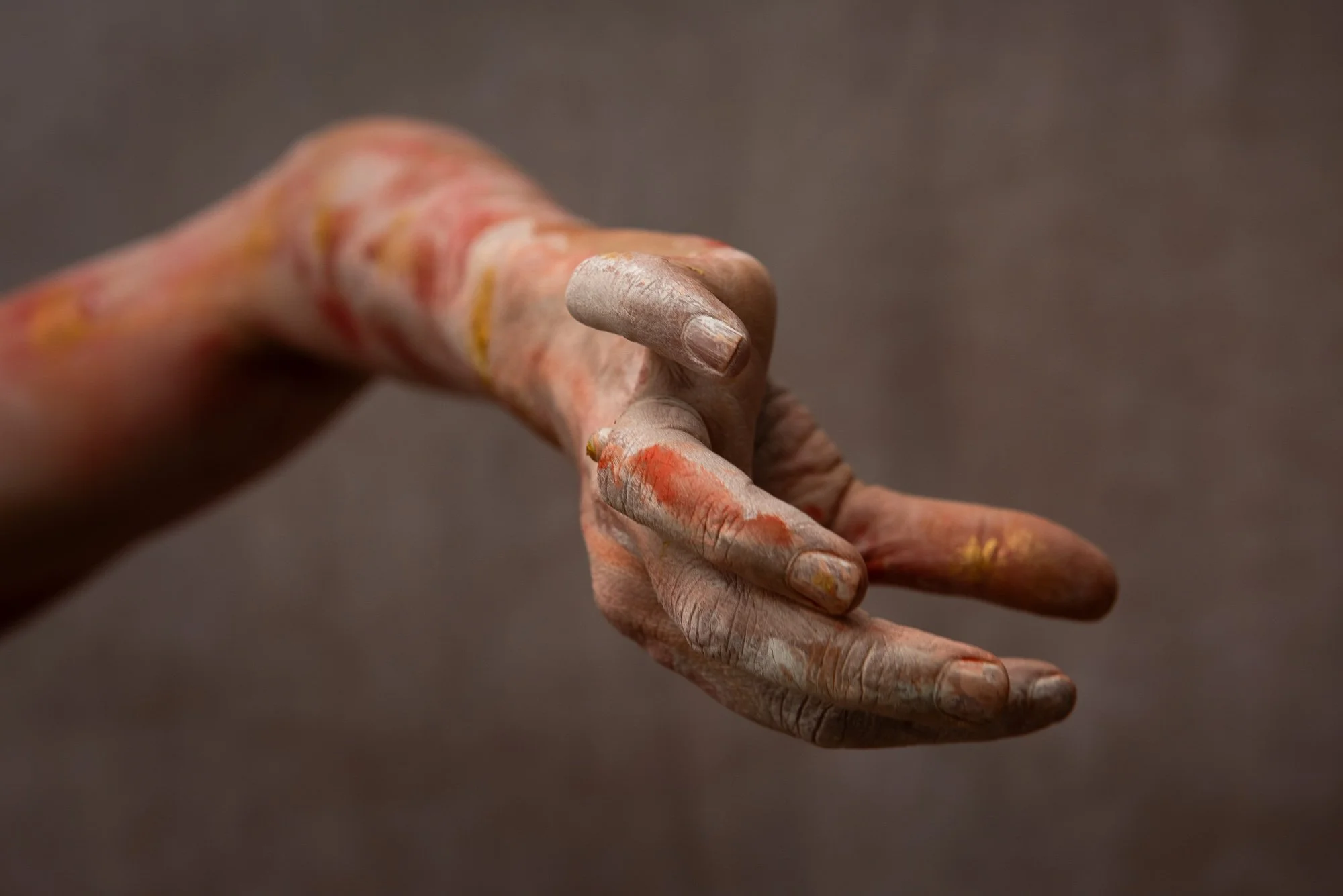 Une main sale et enduite de peinture de différentes couleurs, avec des doigts légèrement pliés contre un fond neutre, lors du stage Regards animé par Isabelle Chapuis et Stéphane Vernier.
