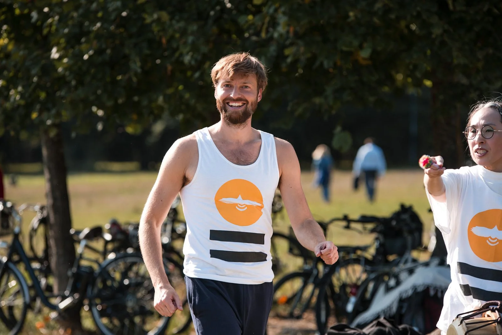 Stéphane Vernier souriant participe à une Planetary Dance à Paris en plein air, avec Dohee Lee, portant un débardeur blanc avec un logo orange et noire.