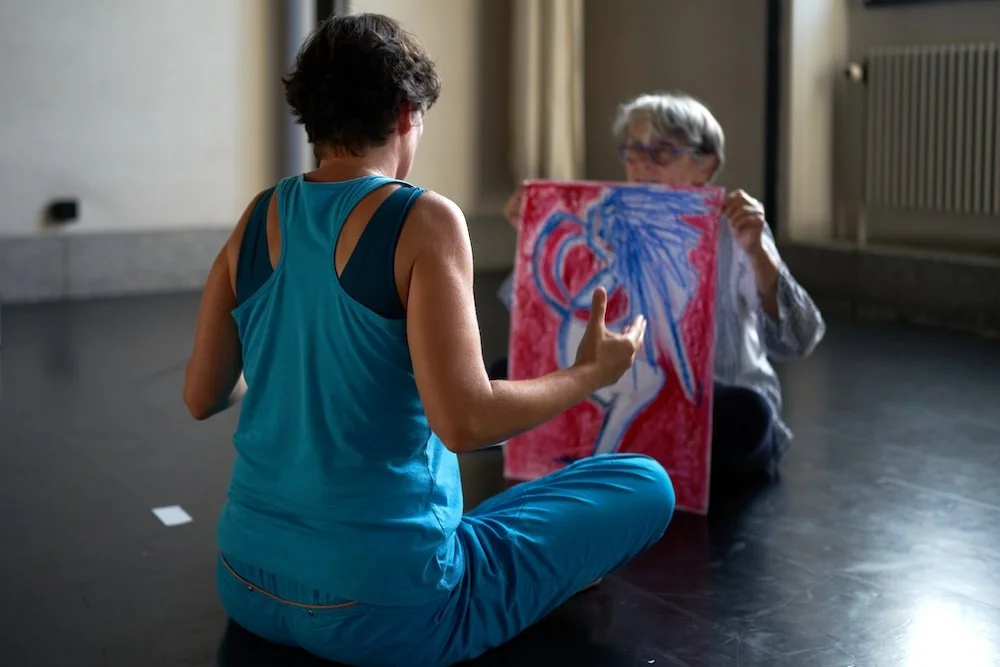 Deux femmes échangeant des informations, l'une avec un tableau d'art coloré lors d'un atelier Life Art Process®.