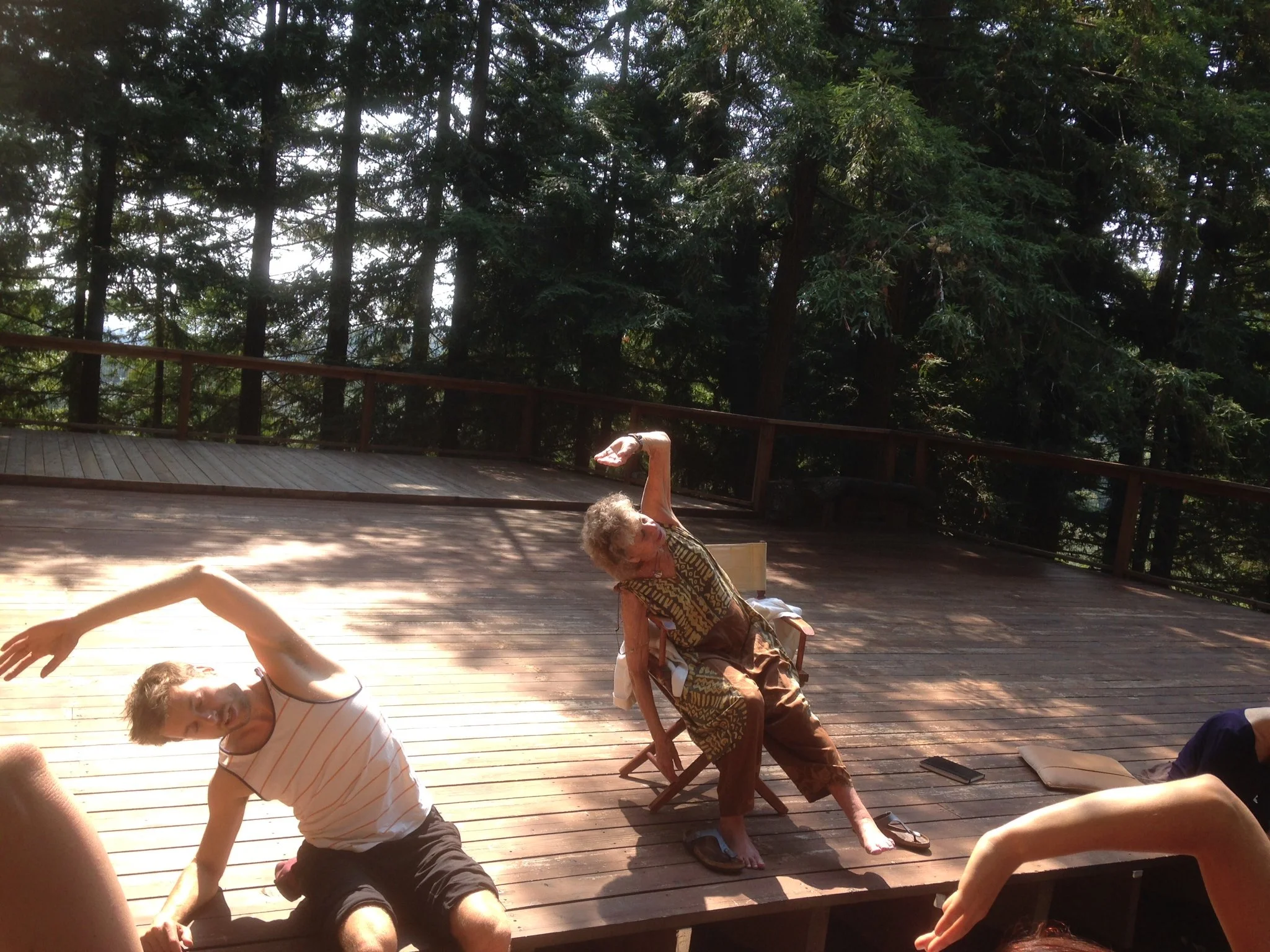 Stéphane Vernier et Anna Halprin sont dans une latéroflexion du buste en miroir à Mountain Home Studio au Tamalpa Institute en Californie, sur la terrasse en bois entourée d'arbres, sous la lumière du soleil.