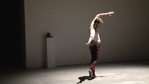 Stéphane Vernier en pleine performance d'Aporia sur un fond sombre, avec un bras étendu et une position corporelle expressive.