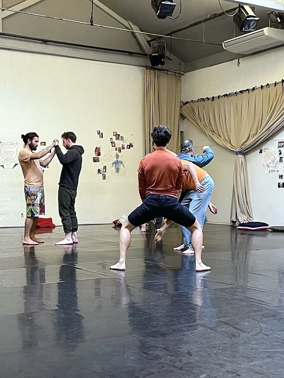 Groupe d'hommes en train de pratiquer la danse dans un studio, quelques personnes sont en position de squat, deux personnes dans le fond semblent échanger ou devoir échanger un objet ou un geste, tous sont pieds nus, pendant le stage Life Art Process