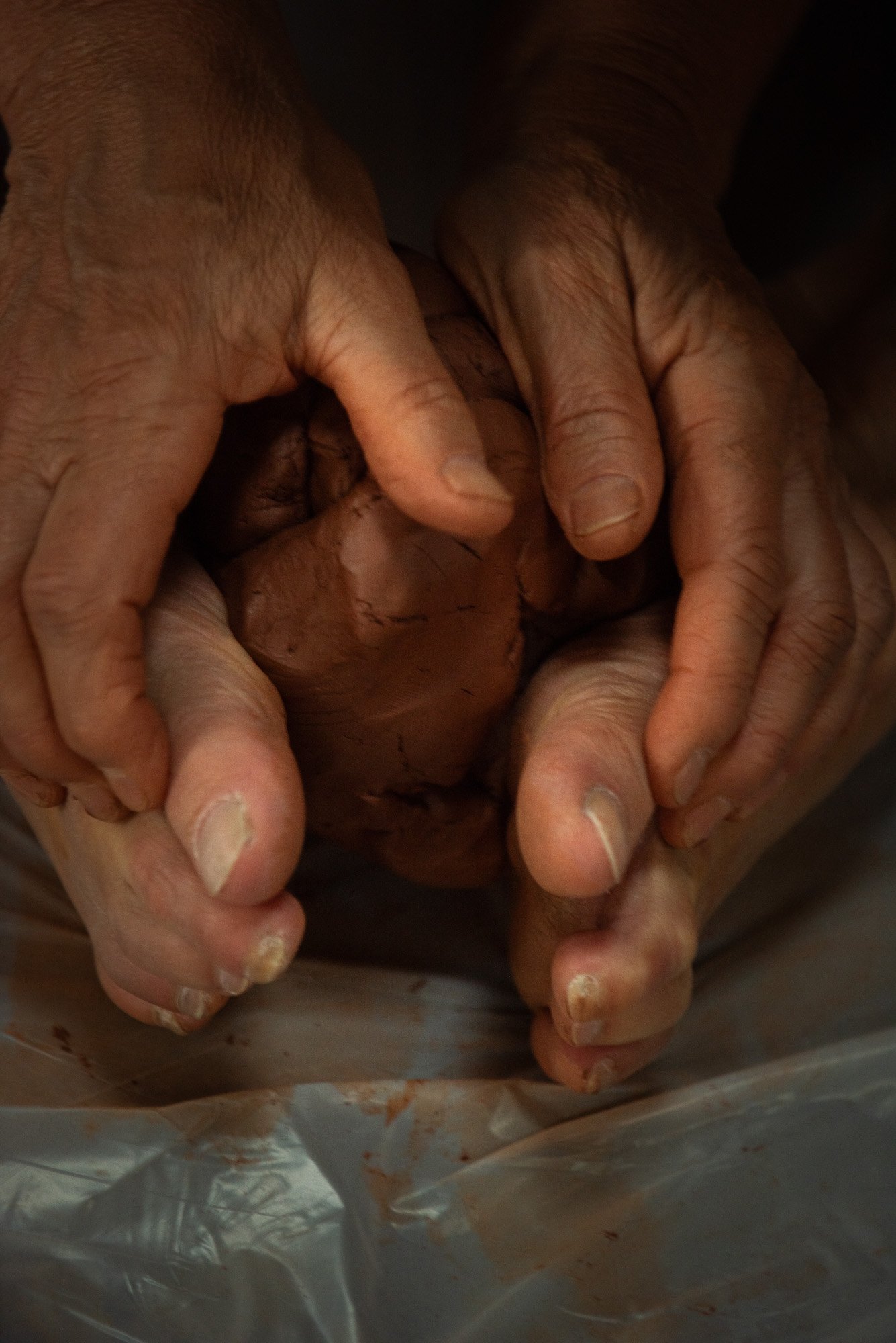 Mains âgées manipulant une boule de pâte ou de terre, avec des traces de couleur rougeâtre, lors du stage Regards animé par Isabelle Chapuis et Stéphane Vernier.
