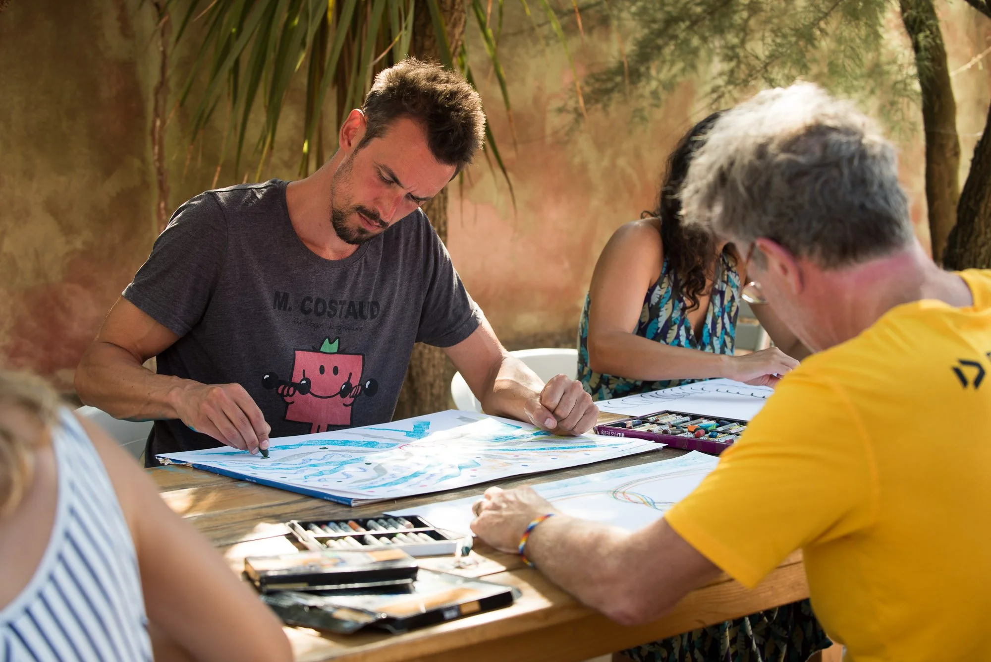 Groupe de personnes dessinant et peignant sur des feuilles lors du stage La Sagesse des Vagues, en plein air, avec un fond de nature et d'arbres.