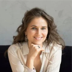 Isabelle Chapuis souriante avec cheveux bouclés, portant une veste beige, posé contre un mur gris.