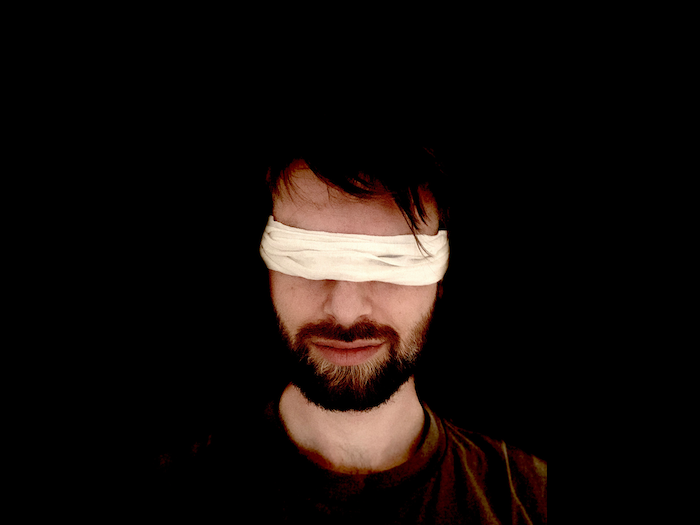 Homme avec une barbe portant un bandeau blanc sur les yeux, dans l'obscurité prêt pour une Blind Dance