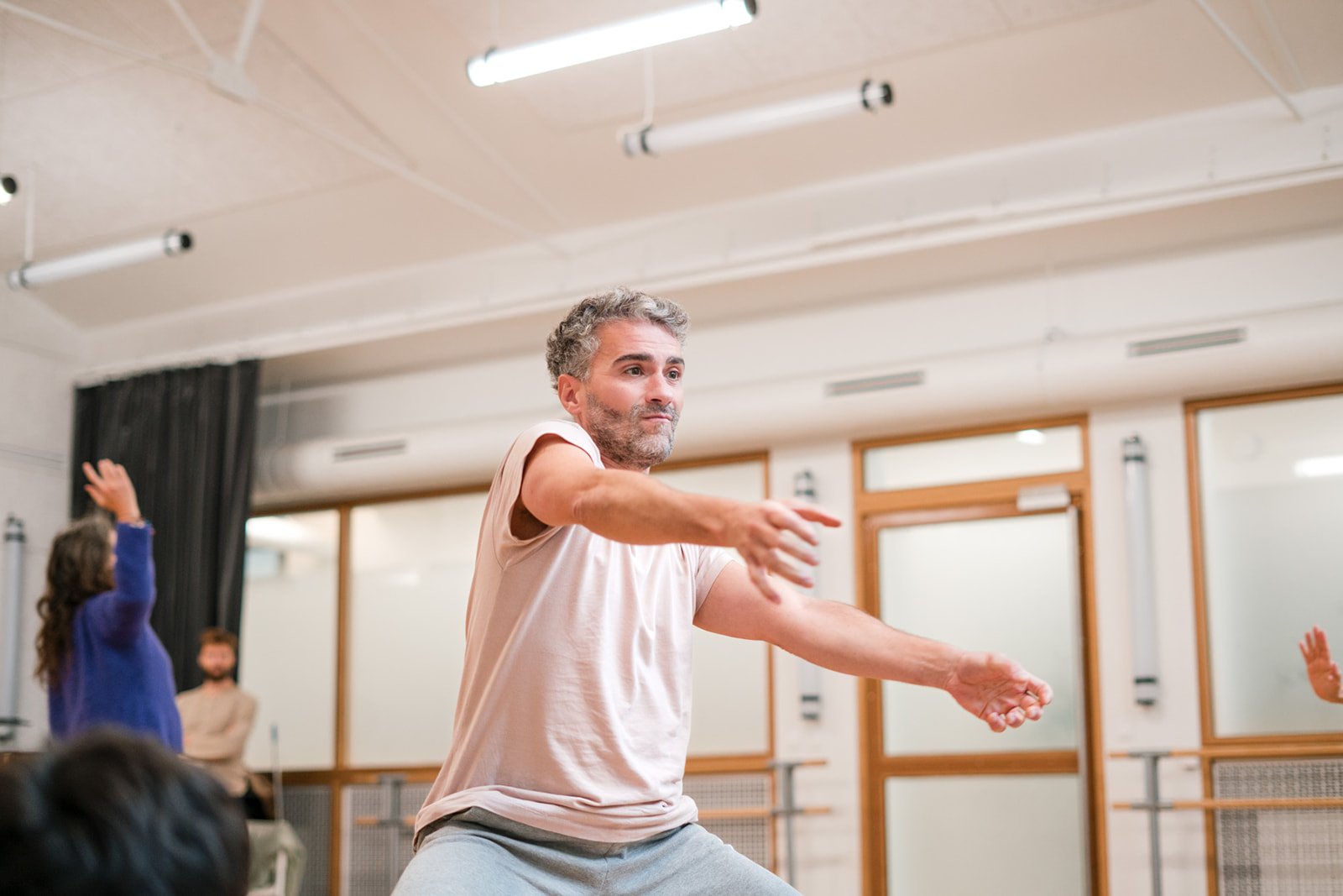 Un homme en train de danser, entouré de plusieurs personnes, certains levant la main, dans une pièce lumineuse avec des fenêtres et des murs blancs, lors des dimanches Life Art Process® de Stéphane Vernier.