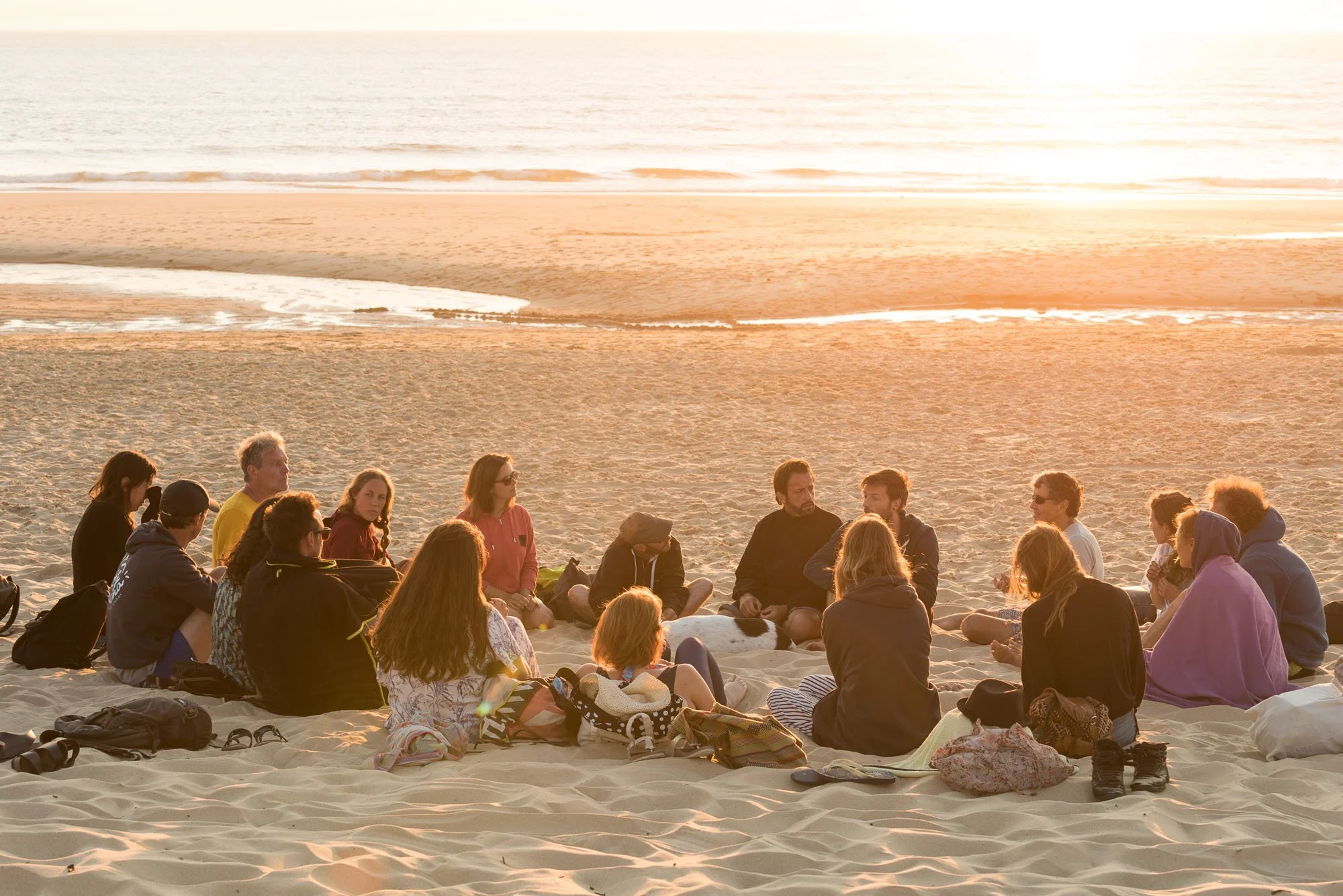 Groupe de personnes assises en cercle sur la plage au coucher du soleil, lors du stage La Sagesse des Vagues.