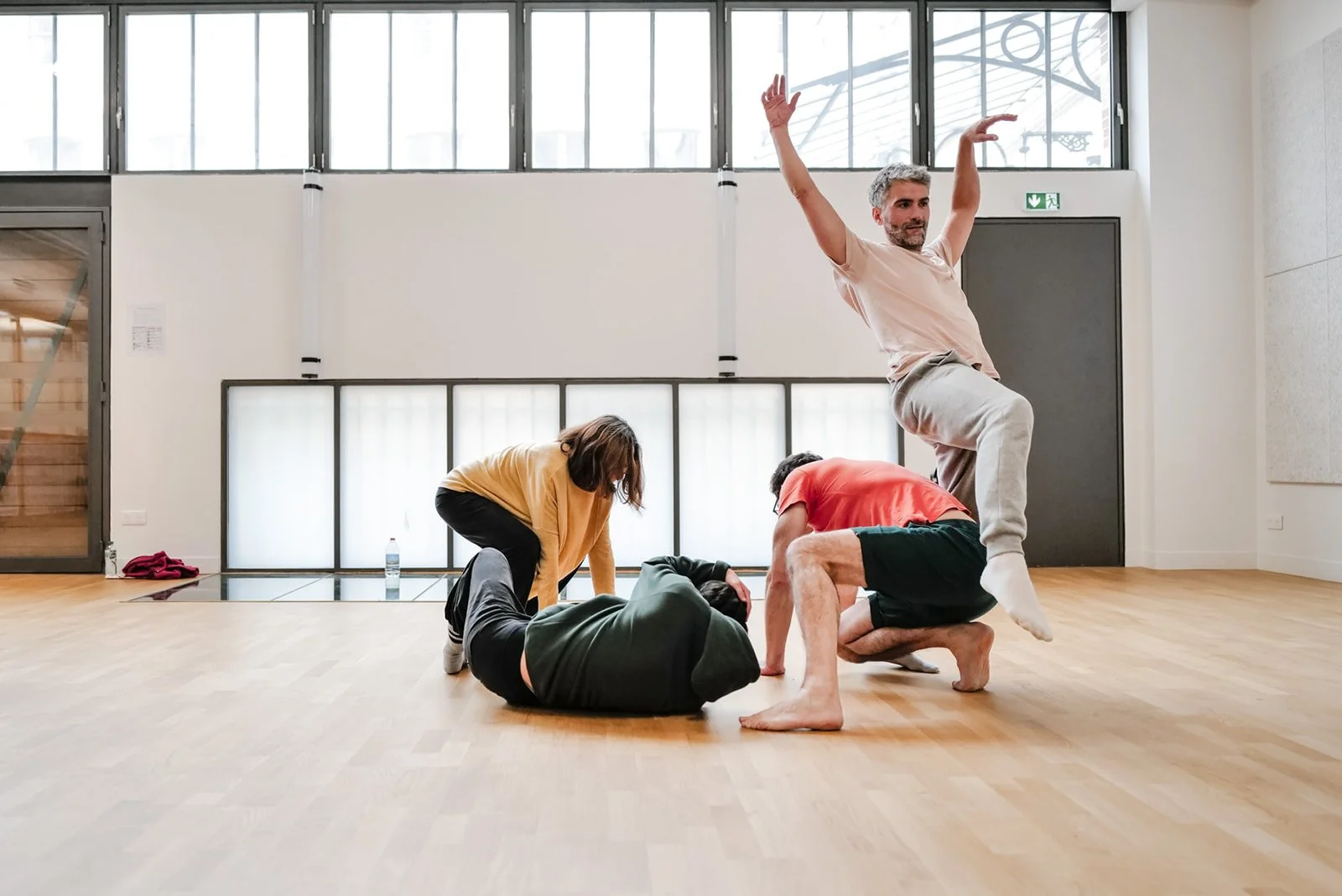 Un groupe de personnes pratiquant le Life Art Process® dans une salle de danse, avec un homme en pleine acrobatie en équilibre sur une jambe, entouré d'autres qui improvisent avec lui.