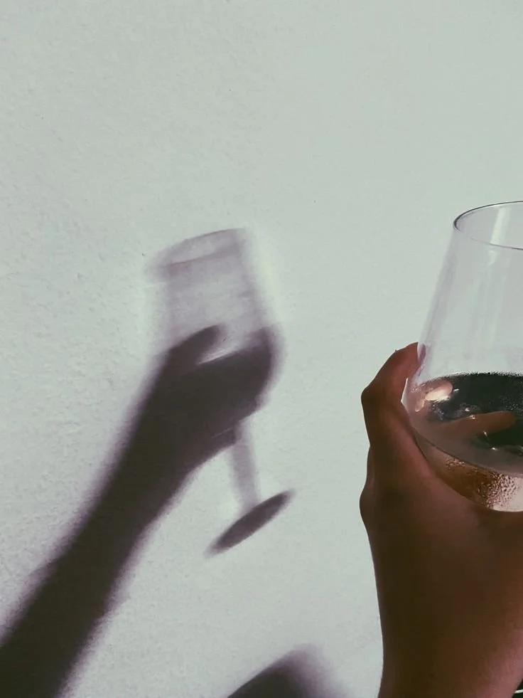 Una mano tiene un bicchiere di vino rosso, la luce crea l'ombra del bicchiere e della mano sulla parete.