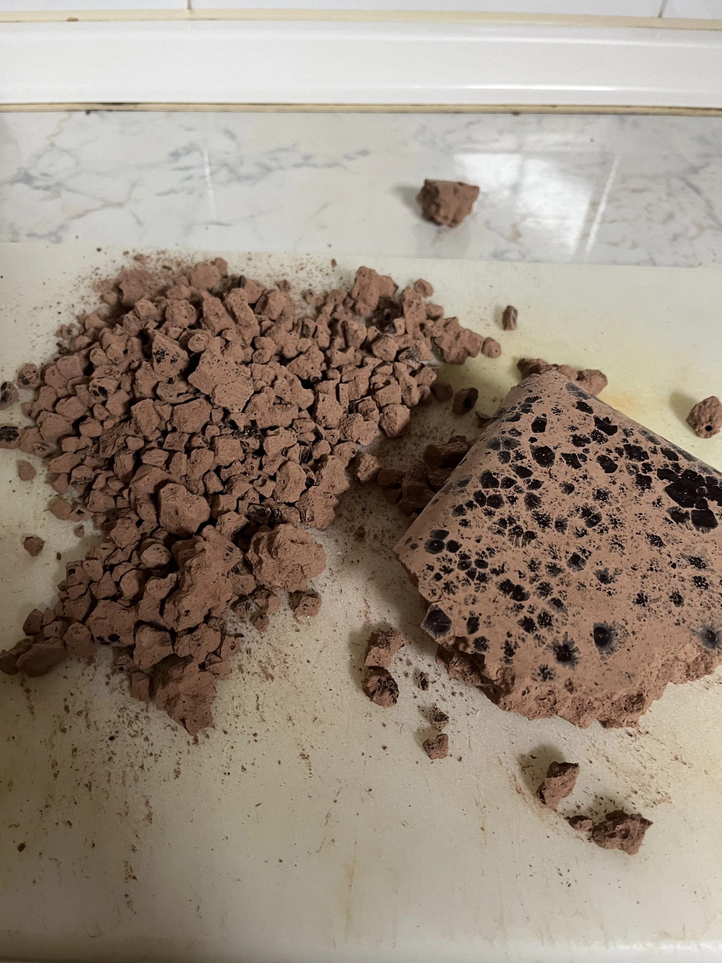 Chopped ceremonial cacao bar with dark spots on a white cutting board.