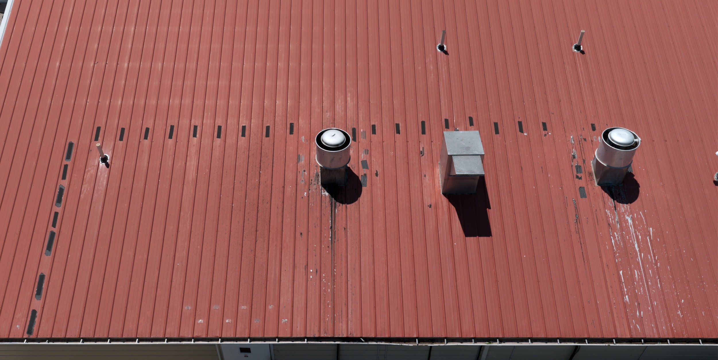A red metal roof with three roof vents and a metal chimney pipe.