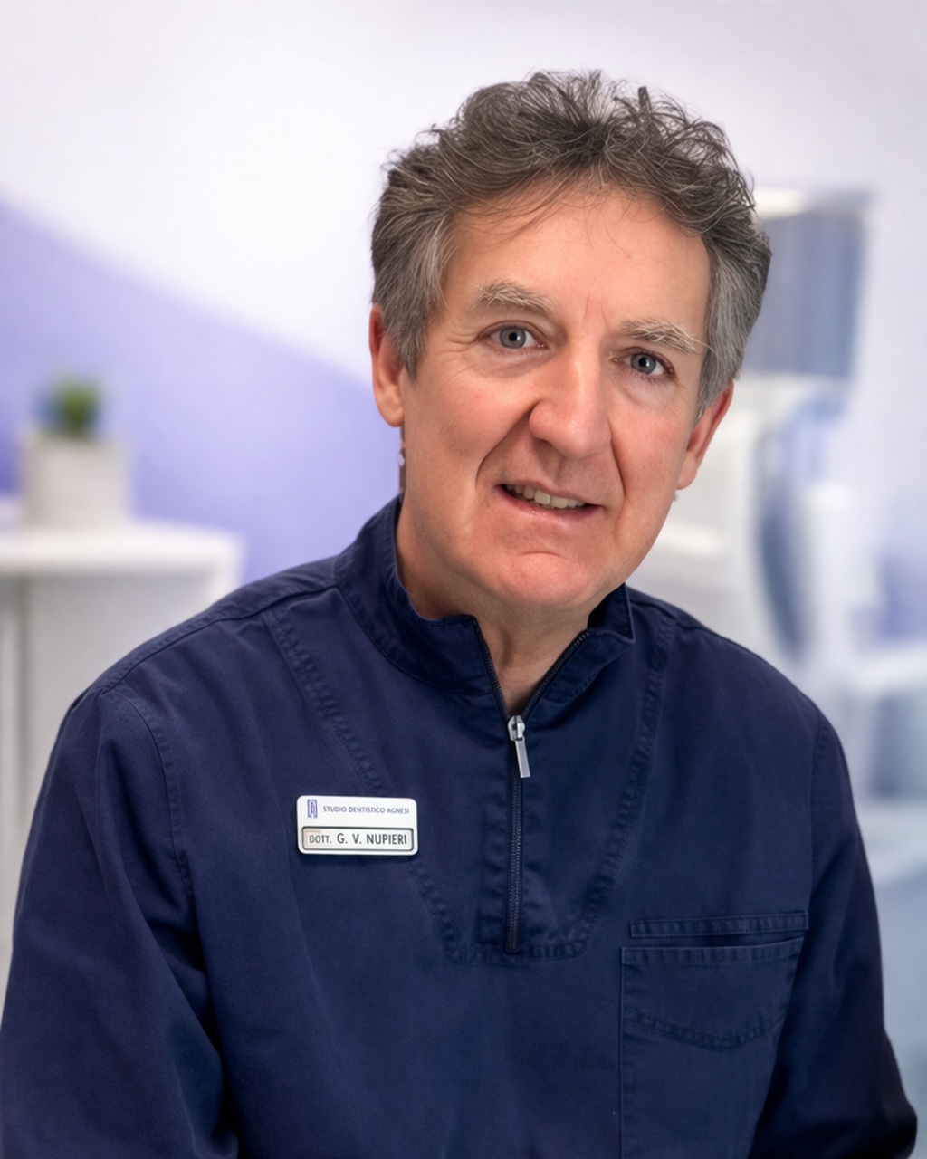 Uomo con capelli grigi e occhi azzurri indossa una divisa da dentista con il nome "G. V. Nupieri".
