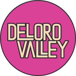 Pink circular logo with the text 'Deloro Valley' in bold, beige-colored letters.