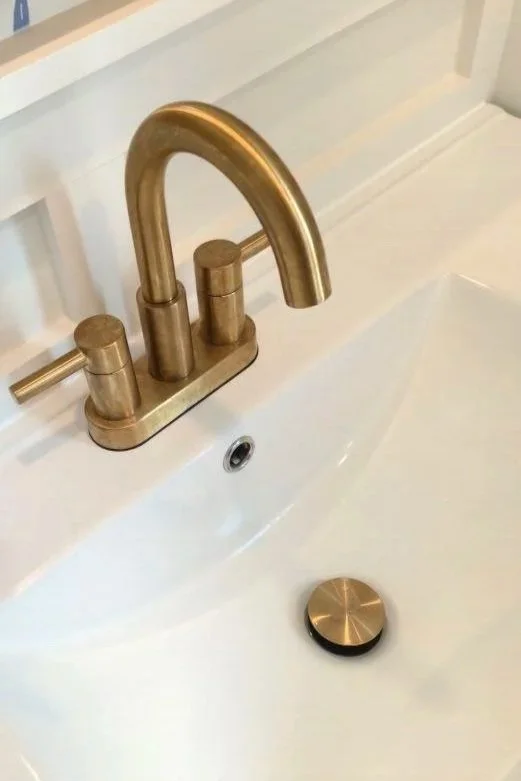 Close-up of a gold bathroom faucet and drain in a white sink.
