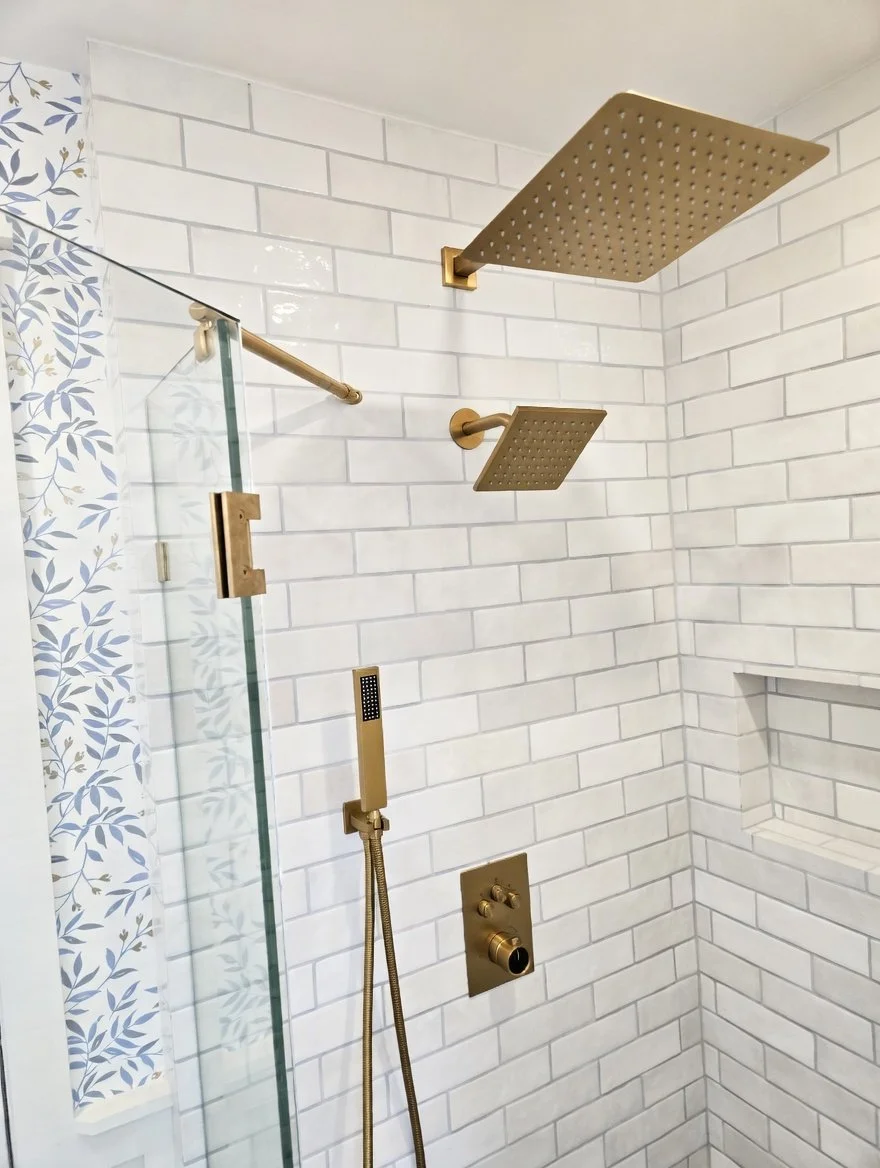 Modern shower with white subway tile walls, brass fixtures, a rainfall showerhead, a handheld shower, and a small recessed shelf.