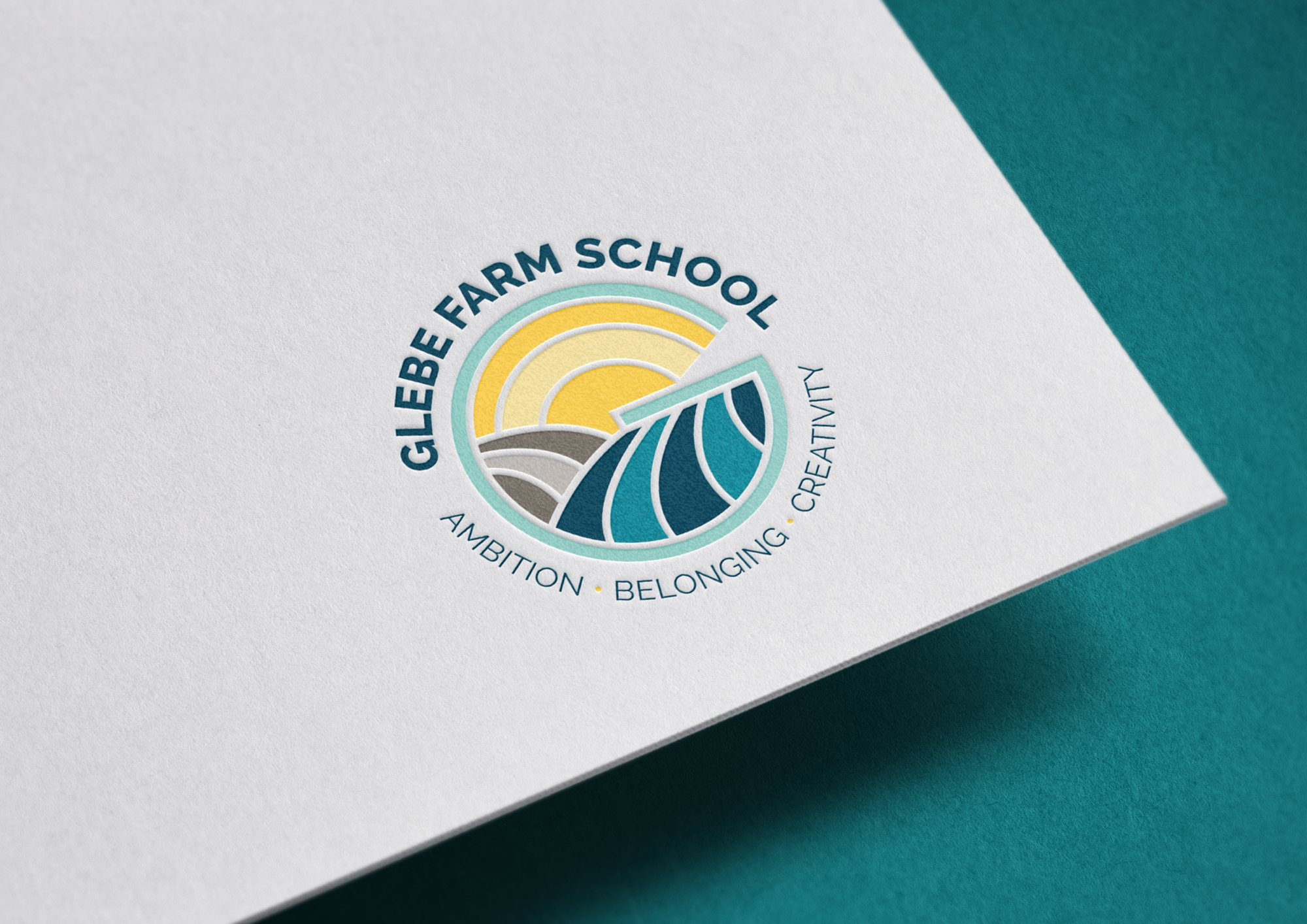 Close-up of a logo on white paper with teal and yellow accents. The logo reads 'Glebe Farm School' and includes a stylized sun, fields, and a leaf. Around the logo are the words 'Ambition, Belonging, Creativity, Growing'.