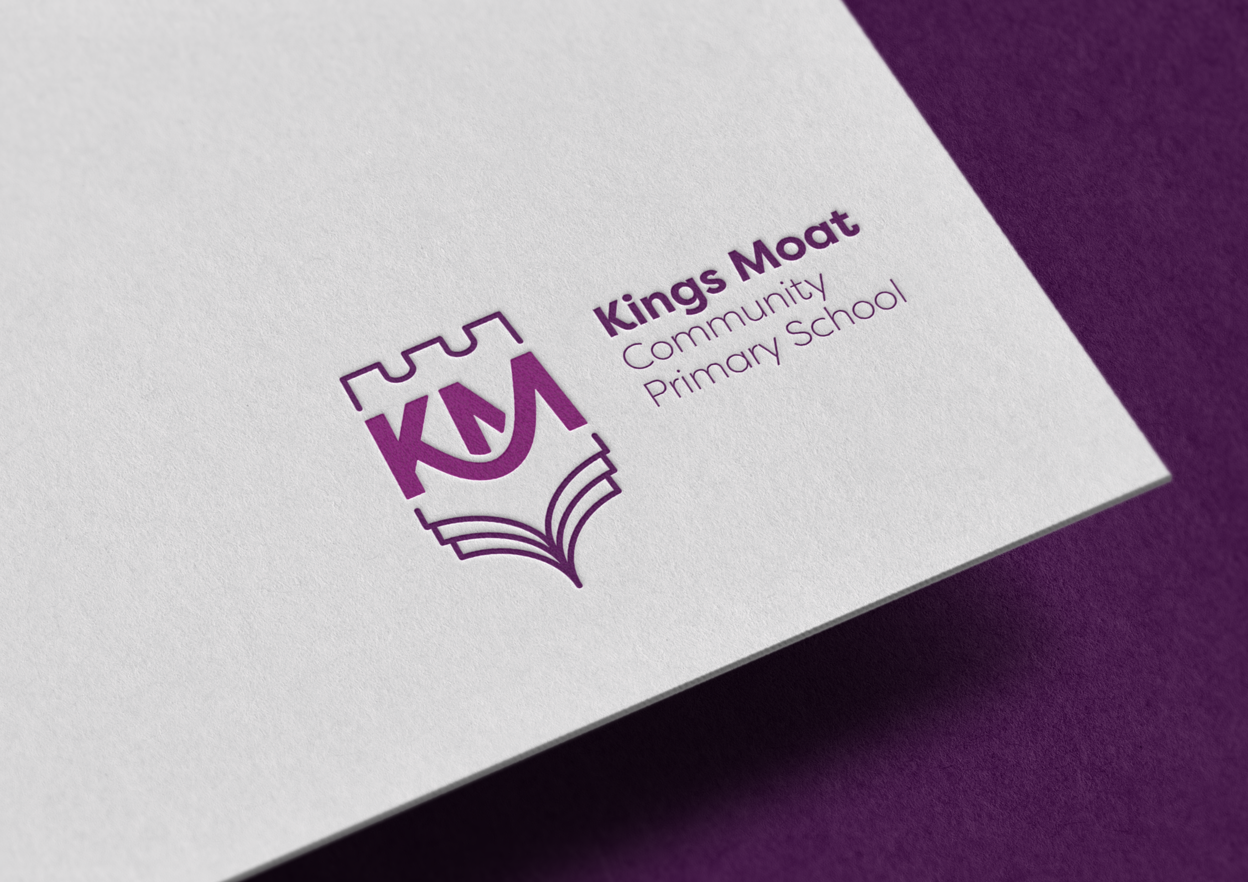 Close-up of a textured paper stock featuring the Kings Moat Community Primary School logo in purple with a castle and open book design on white paper.