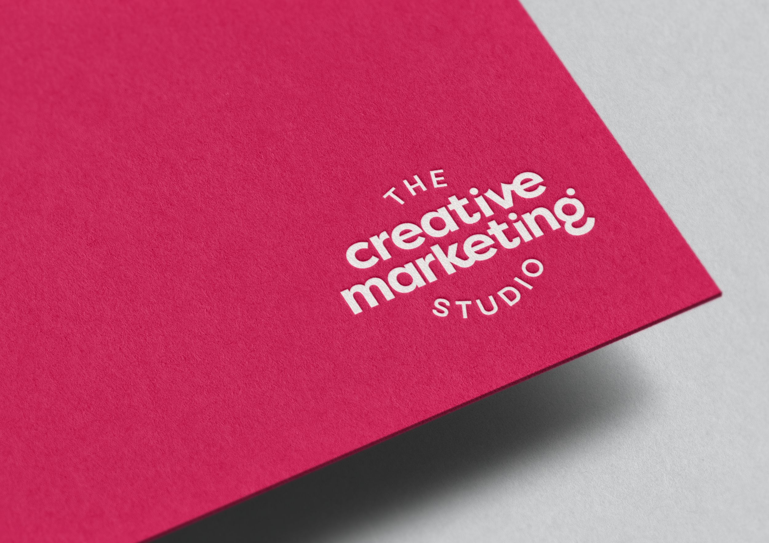 Close-up of a pink textured card stock with 'The Creative Marketing Studio' logo in white.