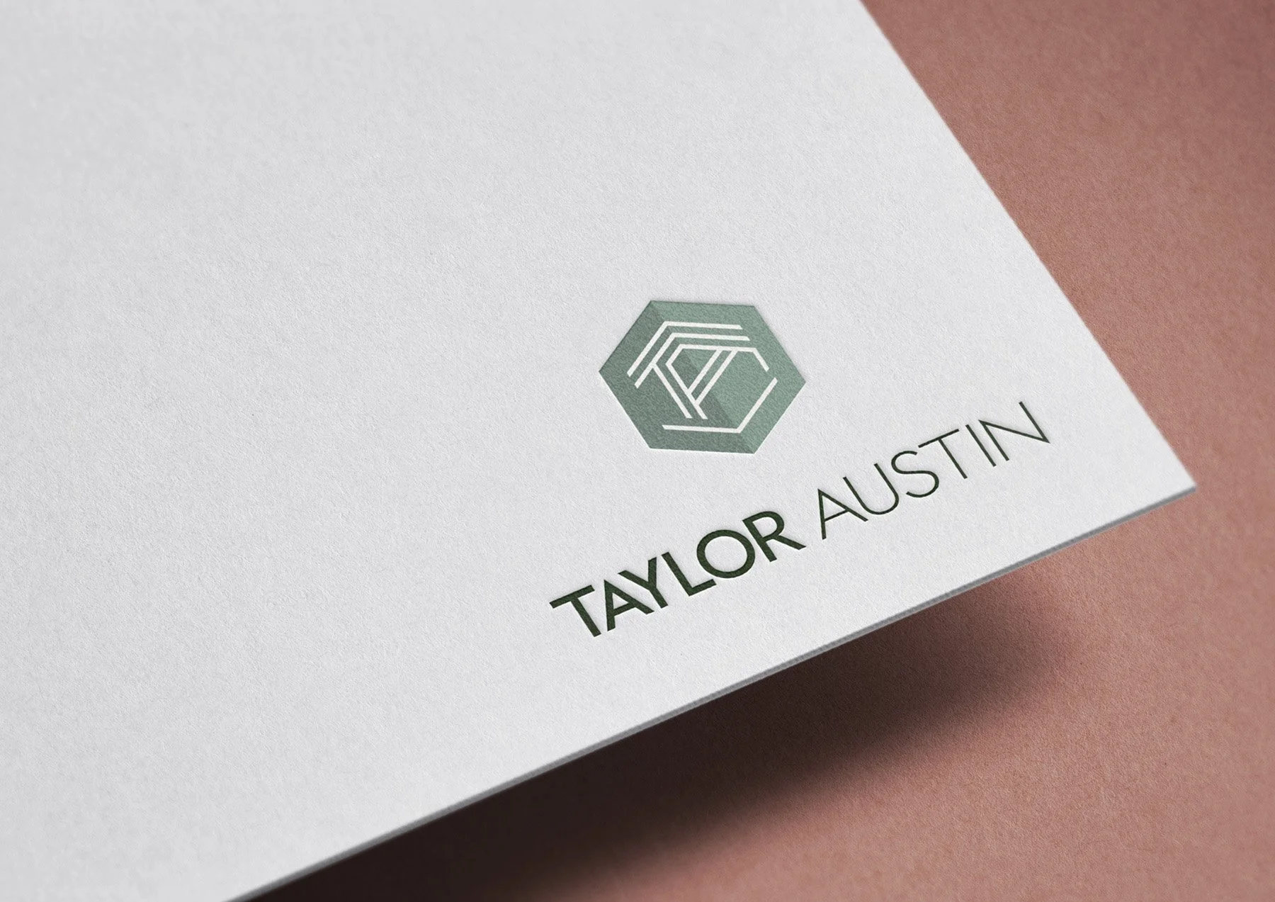 Close-up of a white textured paper with a minimalist logo of a hexagon and geometric lines, and the text 'TAYLOR AUSTIN' printed below.