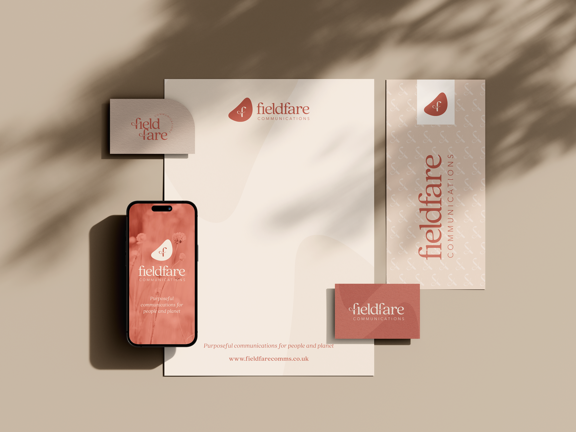 Display of branding materials for Fieldfare Communications, including a smartphone with the company's logo and slogan, business cards, and banners with the company's logo and website, all in beige and reddish tones.
