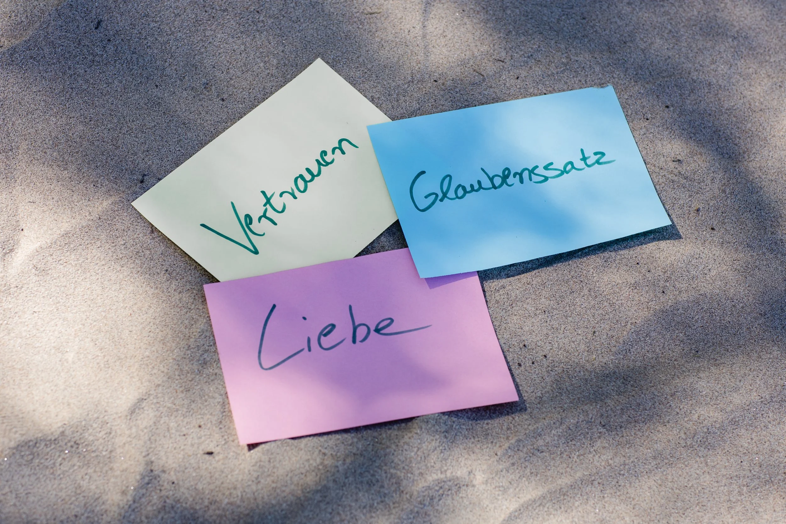 Lösungen finden bei Lebenskonflikten und Erschöpfungsphasen. Drei farbige Post-it-Notizen liegen auf sandigen Untergrund.