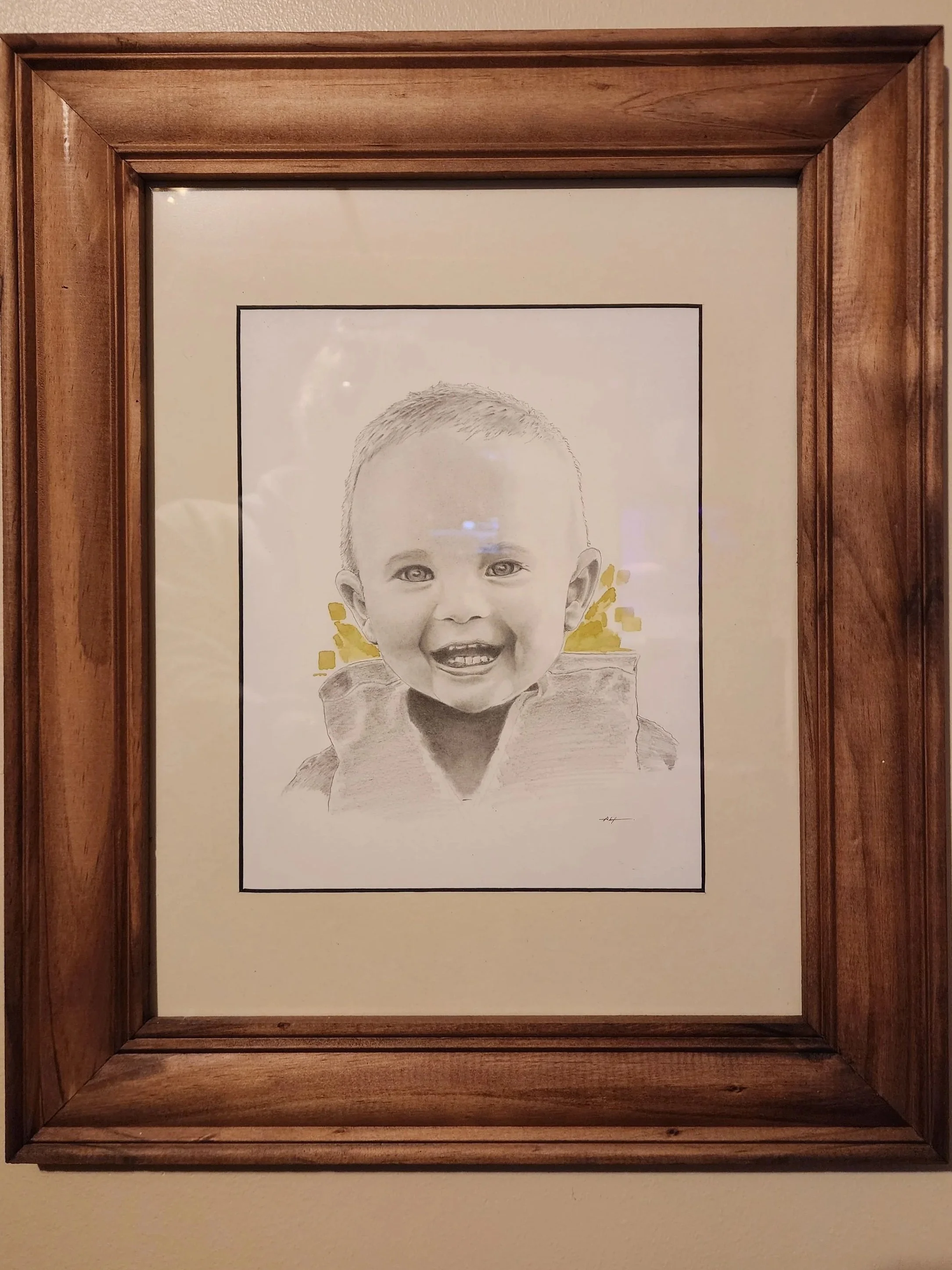 A framed black-and-white portrait of a young boy with short hair, smiling with an open mouth, surrounded by a decorative gold pattern.