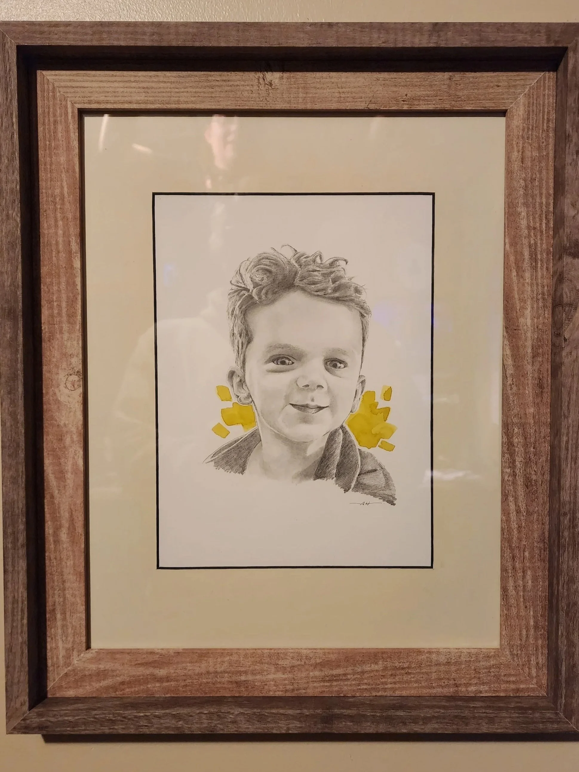 A framed artwork of a smiling young child's face sketched in black and white with yellow accents behind the head, in a wooden frame.