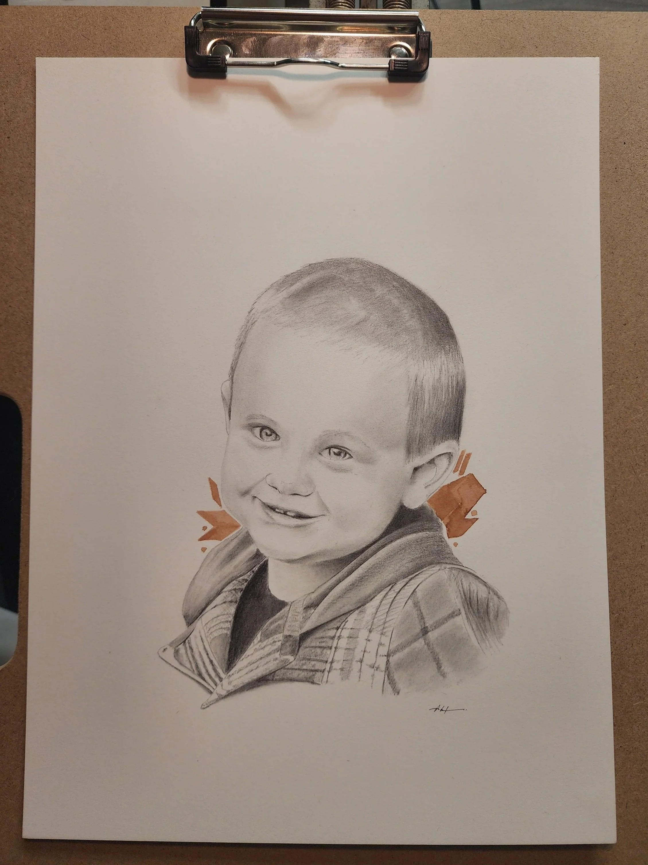 A detailed graphite pencil portrait of a young boy with short hair, smiling, wearing a hooded jacket with a plaid pattern on the sleeves, and illustrated with shading and highlights to depict facial features.