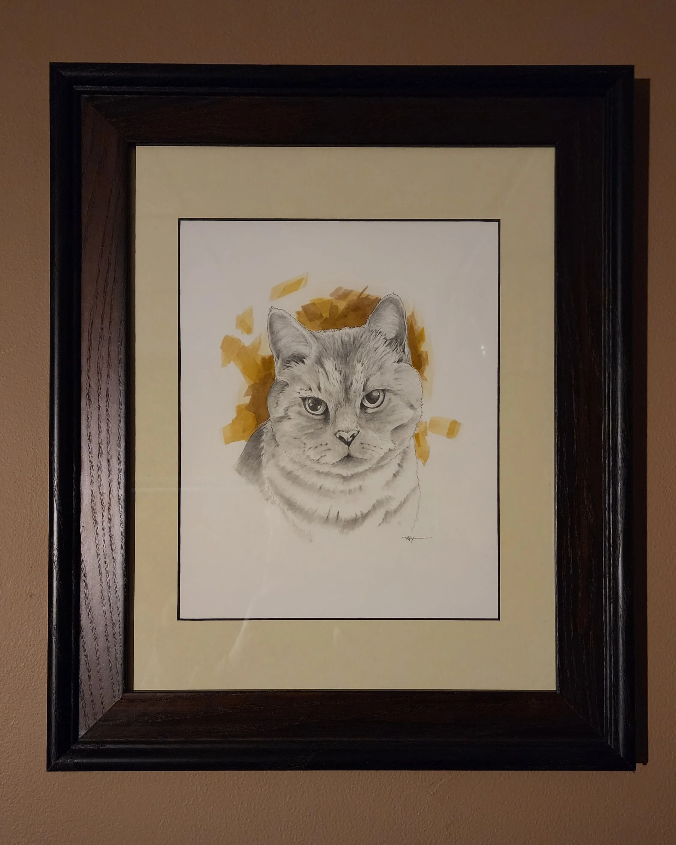 Framed watercolor painting of a gray cat with a yellow and orange abstract background on a brown wall.