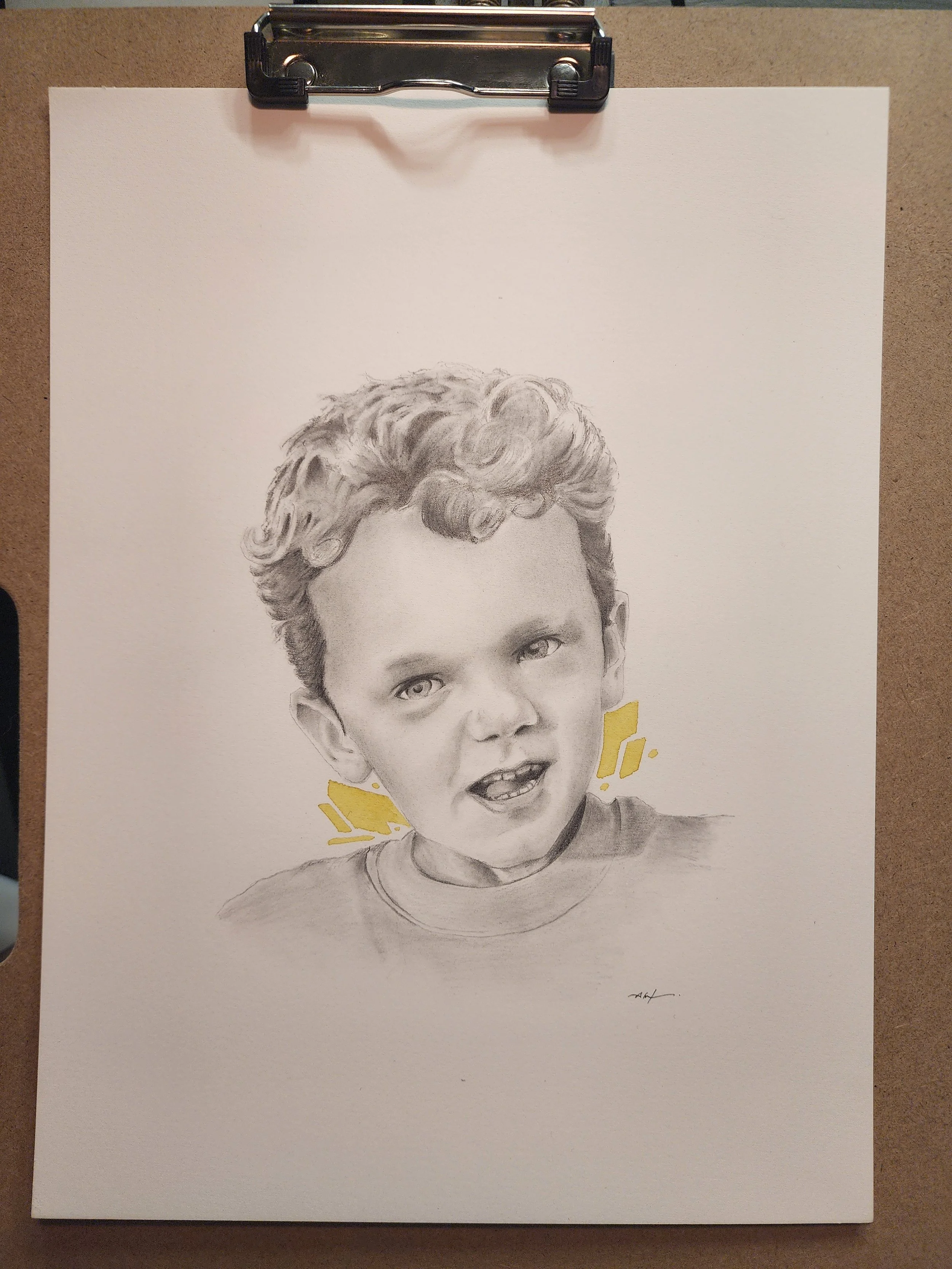 A realistic pencil drawing of a young boy with curly hair and expressive eyes, with yellow accents around his neck and shoulder area.