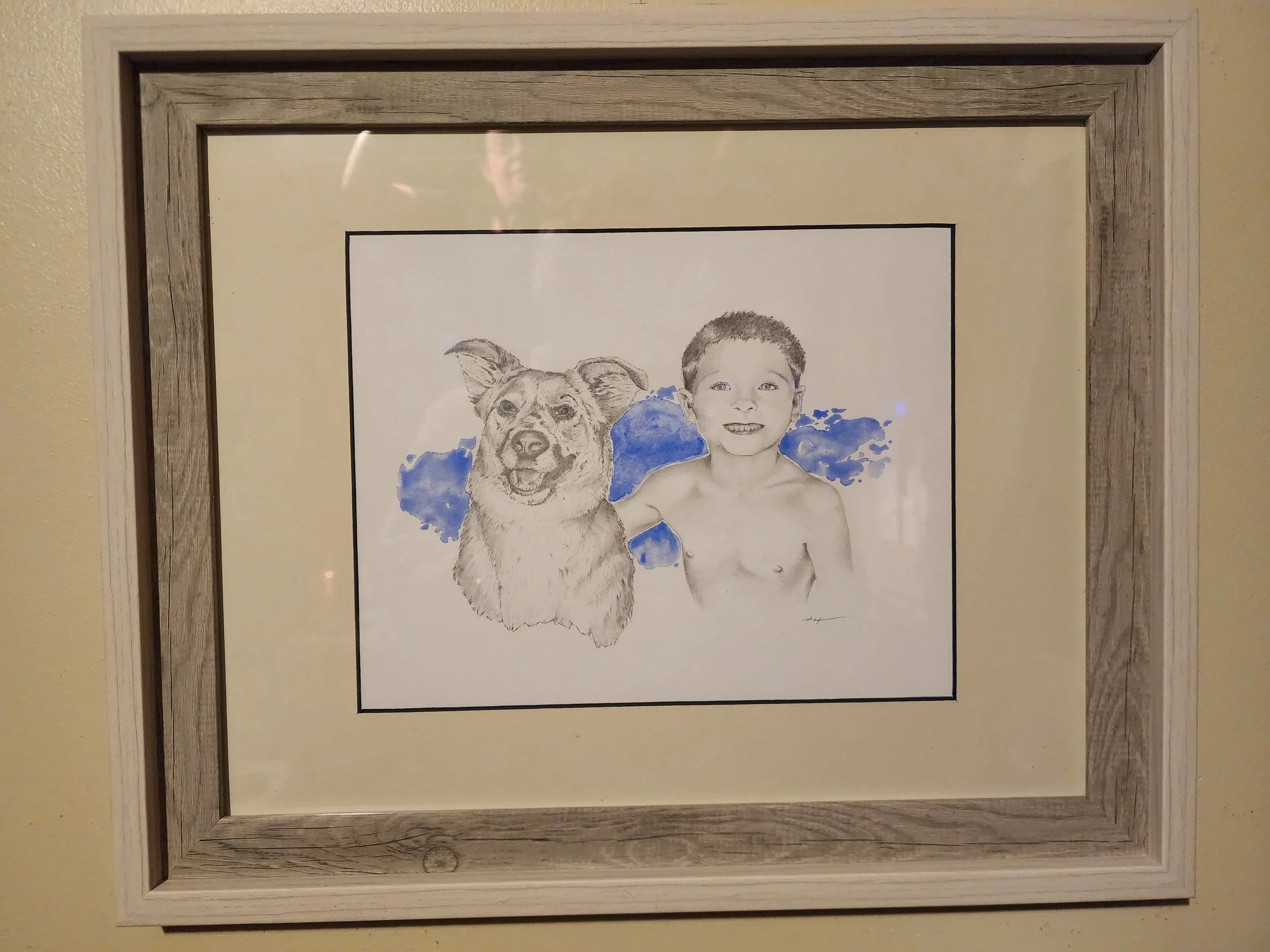 Framed watercolor and graphite painting of a young boy smiling and with his dog, with blue watercolor splashes背景.