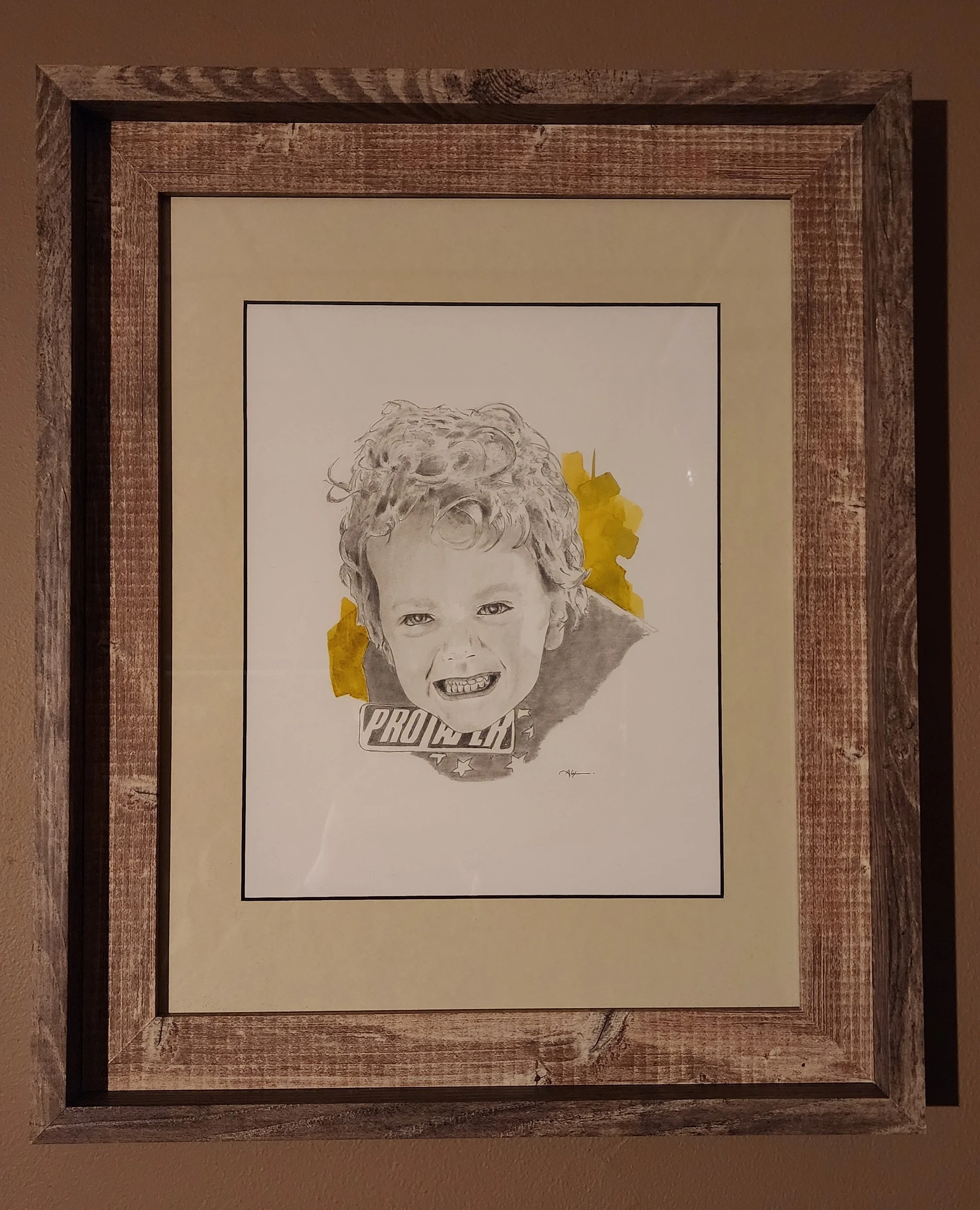 A framed black-and-white portrait of a young boy with curly hair, smiling widely, with yellow paint splashes around his face