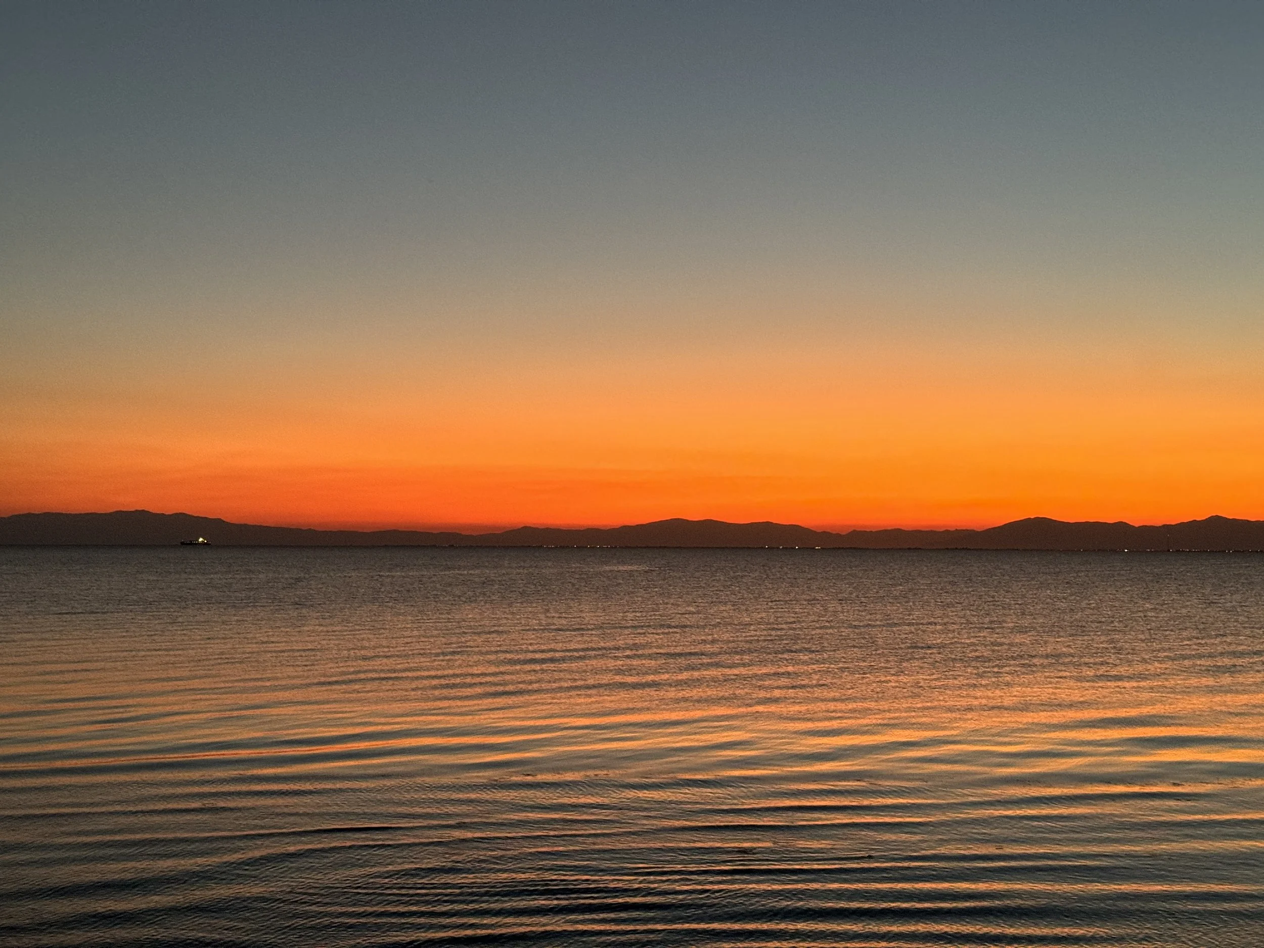 Sunset over a calm body of water with a distant mountain range on the horizon.